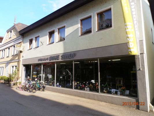 Obchod s bicyklami na malej ulici s niekoľkými bicyklami pred výkladom.