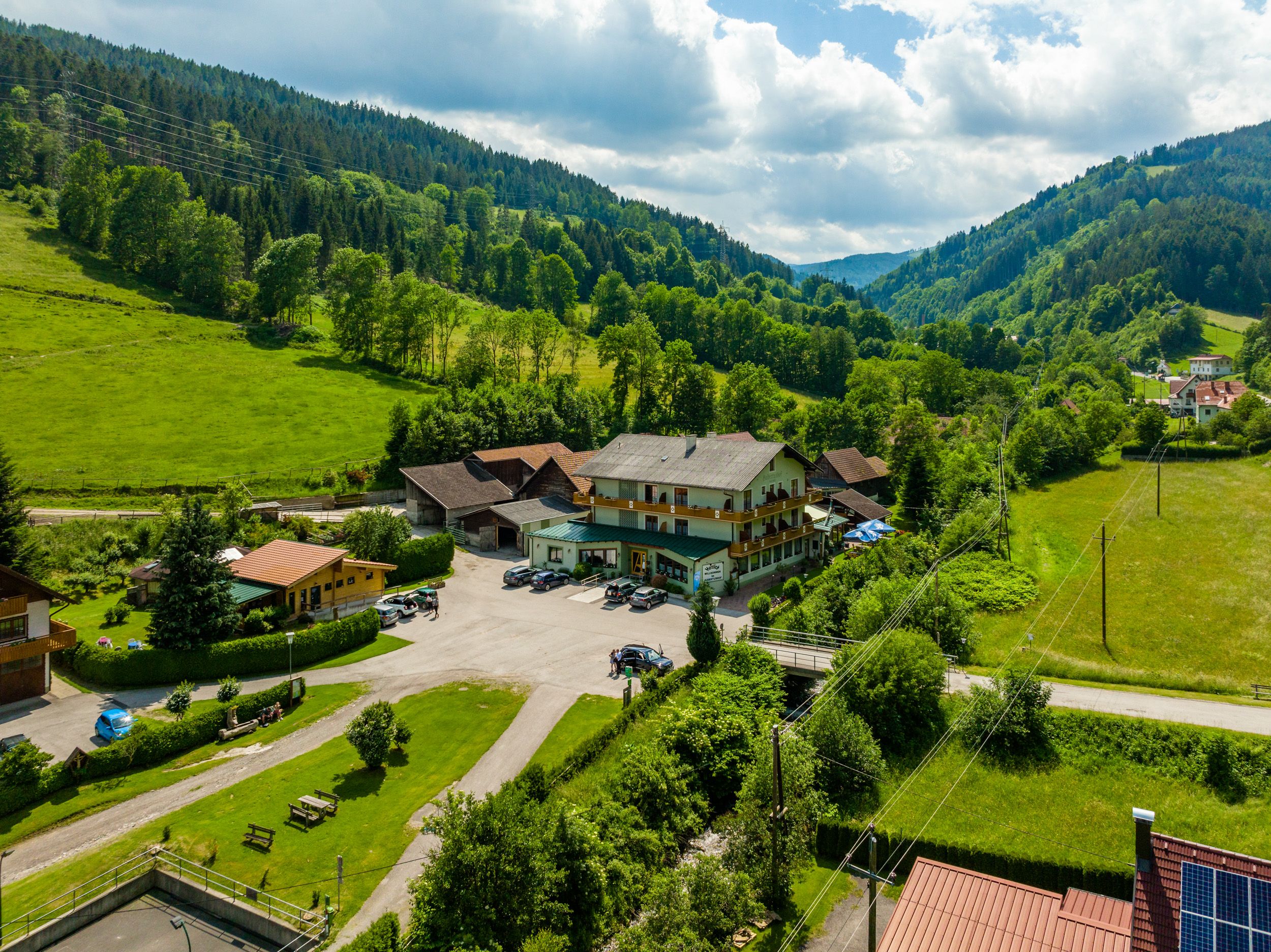 Vidiecka krajina s veľkou budovou obklopenou zelenými kopcami a stromami.