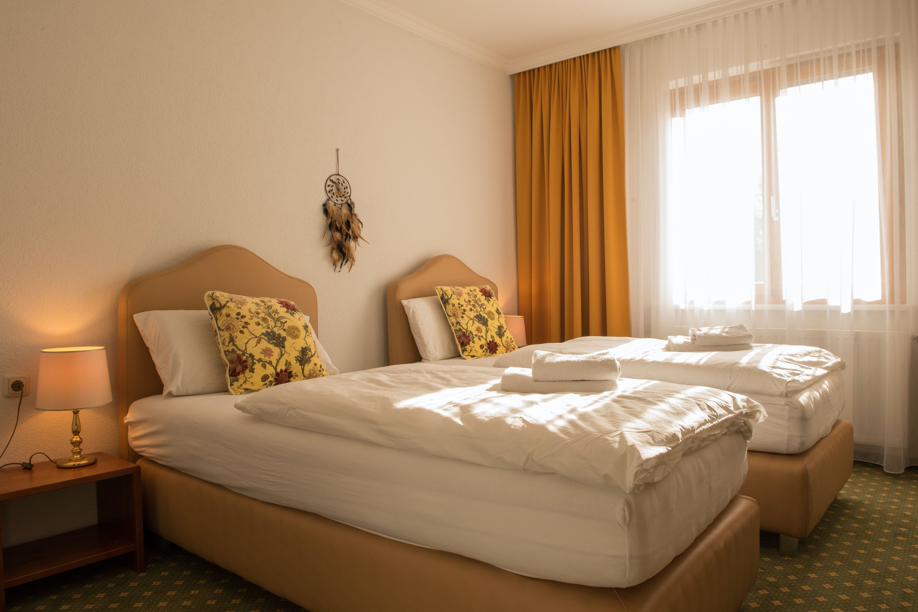 Útulná dvojlôžková izba s dvoma samostatnými posteľami, žltými závesmi a lapačom snov na stene.