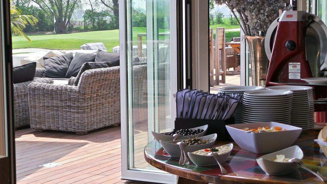 Stôl s riadom a občerstvením vedľa terasy s ratanovým nábytkom a výhľadom na zelený trávnik.