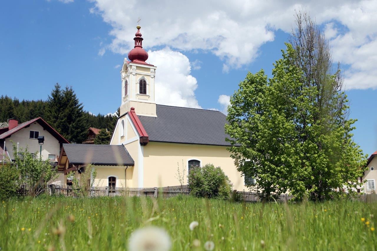 Kostol v Mitterbachu s červenou vežou a zeleným stromom v popredí.