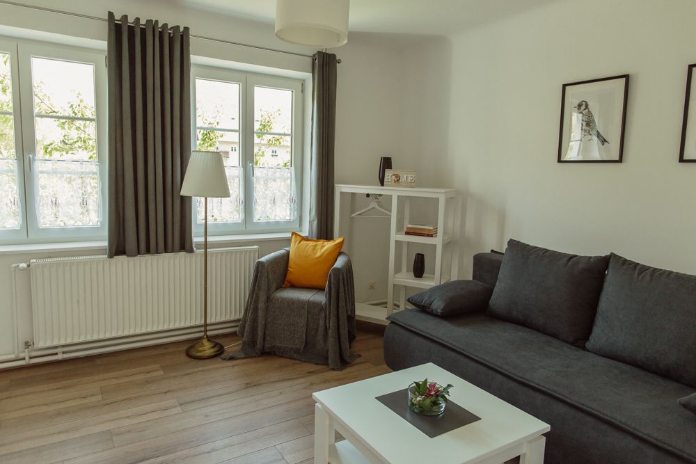 Svetlá obývacia izba so sivou pohovkou, kreslom, stojacou lampou a bielym nábytkom.