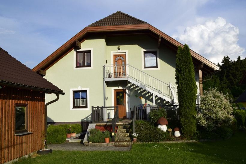 Dvojposchodový dom so zeleným náterom a vonkajším schodiskom v záhrade.