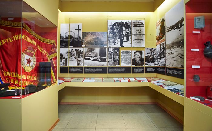 Výstavná miestnosť s historickými fotografiami, dokumentmi a červenou vlajkou.