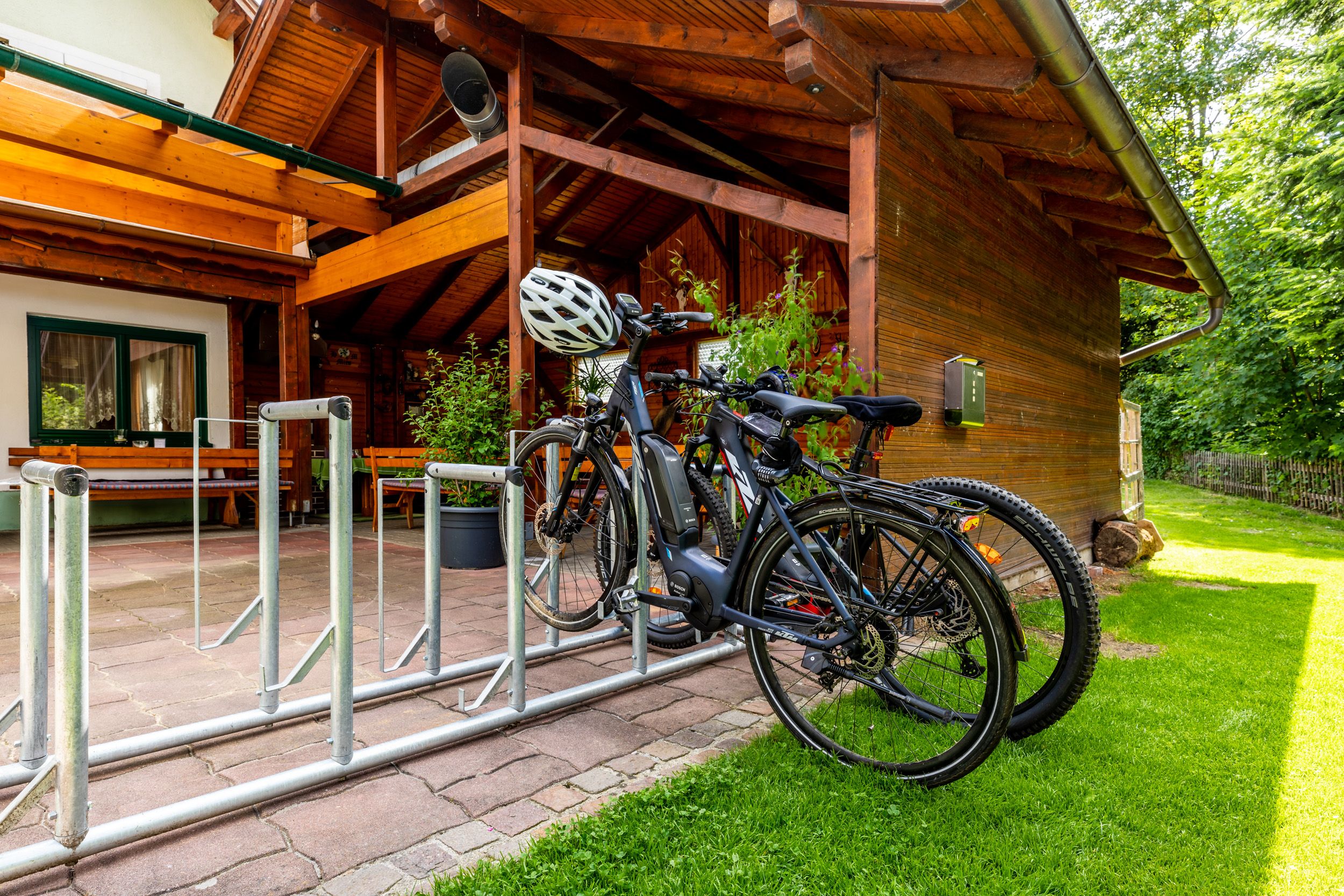 Bicykle v stojane na bicykle pred drevenou budovou s terasou.