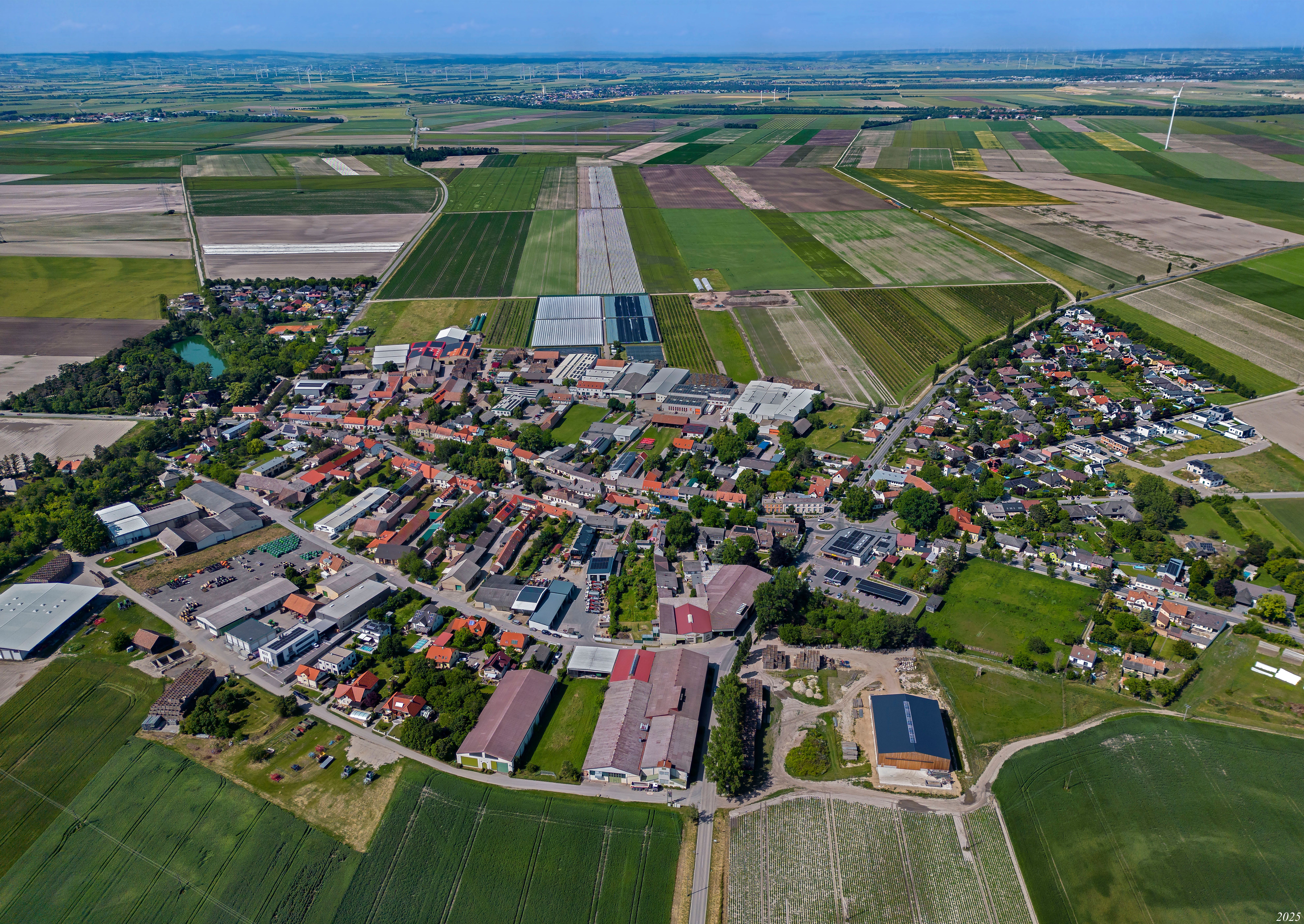 Letecký pohľad na Raasdorf s centrom obce, poľami, skleníkmi a veternými turbínami v okolí.