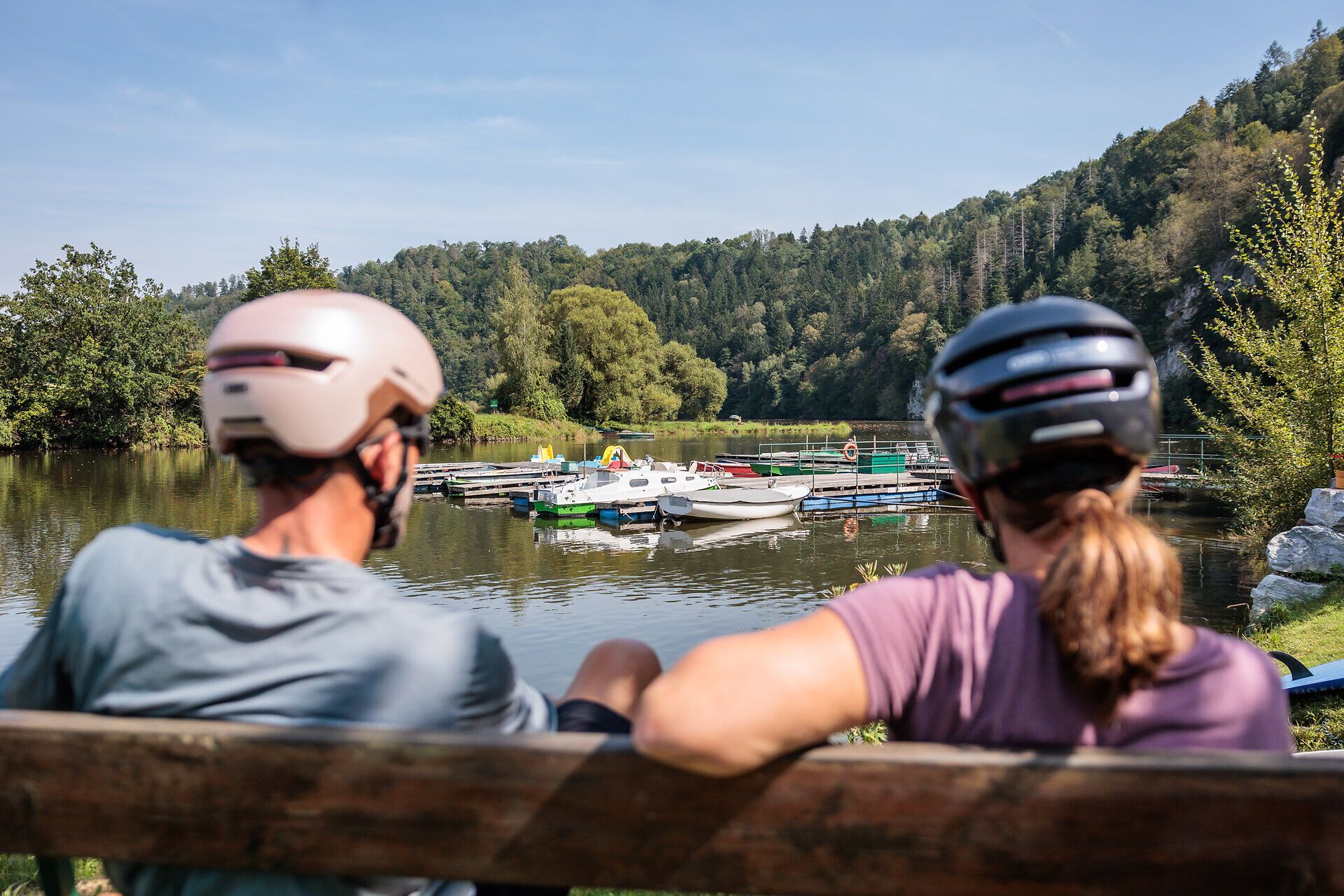 Jemný vánok hladí lesknúcu sa nádrž, zatiaľ čo cyklisti oddychujú na lavičke a vychutnávajú si malebnú krajinu. Toto miesto obklopené sviežou zeleňou a kopcami vás pozýva na oddych a spoznávanie krás prírody.