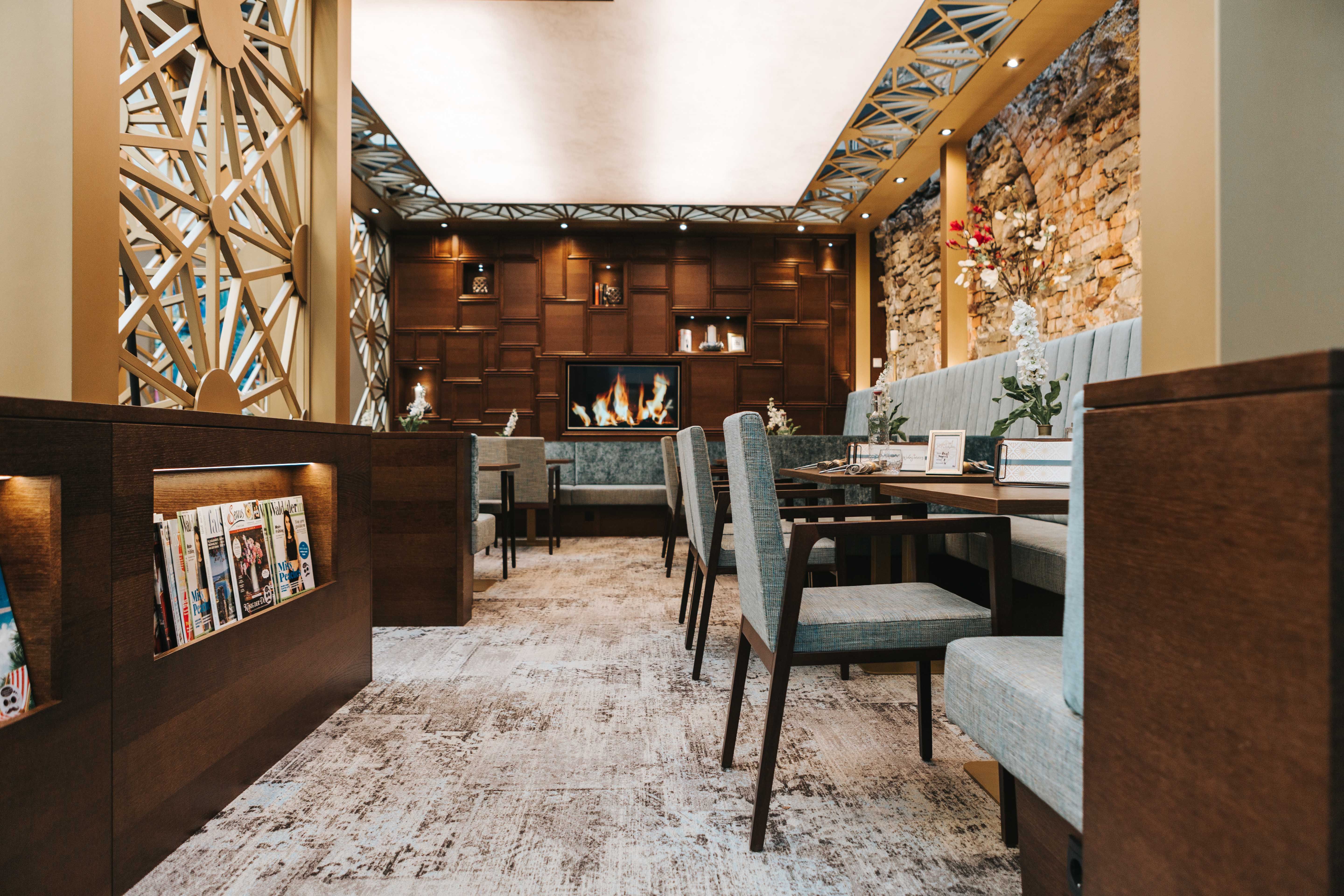 Pohľad do interiéru štýlovej kaviarne s útulným sedením, krbom a stojanom na časopisy.