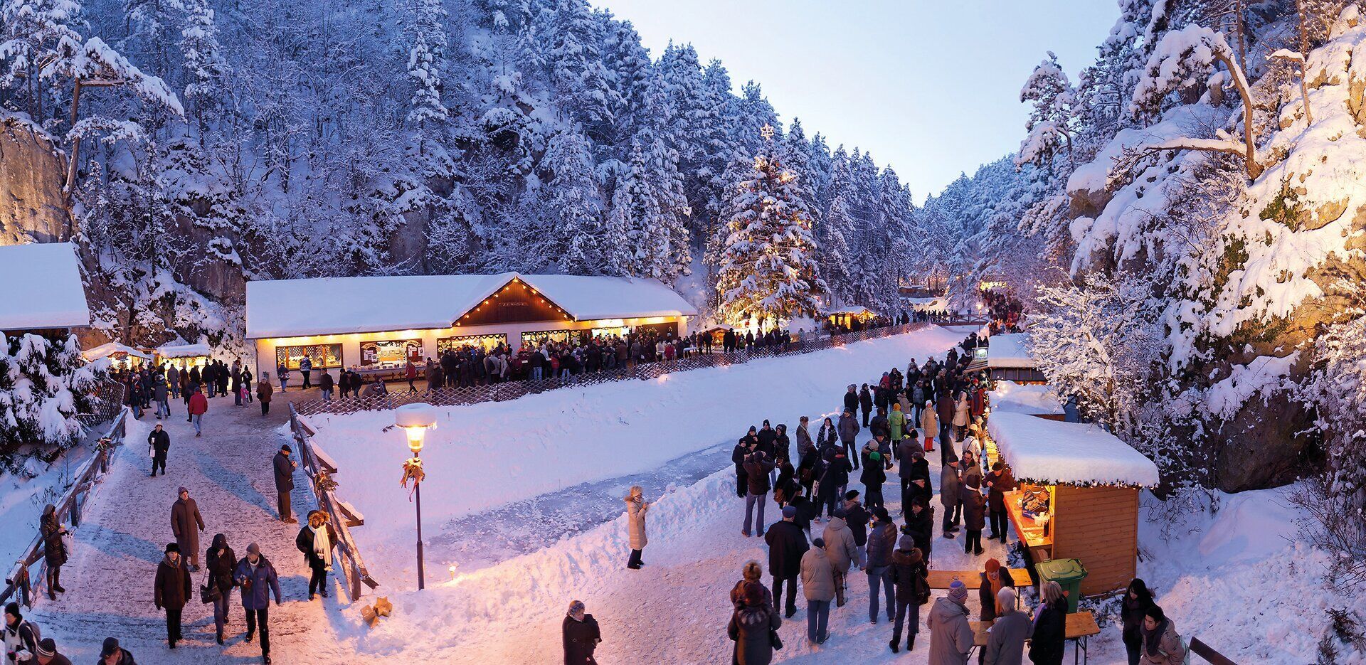 In der malerischen Winterlandschaft der Johannesbachklamm erstrahlen die festlich geschmückten Stände im warmen Licht der Adventszeit. Die schneebedeckten Bäume umrahmen die fröhlichen Besucher, die sich bei Glühwein und regionalen Köstlichkeiten auf die besinnliche Zeit einstimmen.
