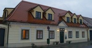 Dvojpodlažná budova so žltou fasádou a červenou strechou.