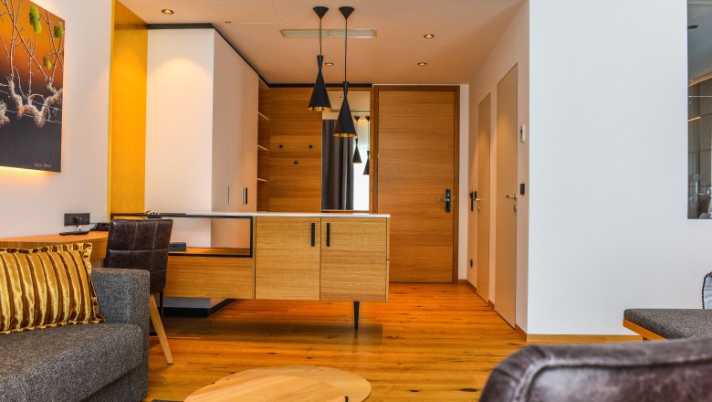 Pohľad do interi&eacute;ru modern&eacute;ho hotelov&eacute;ho apartm&aacute;nu s drevenou podlahou, sivou pohovkou a dreven&yacute;m stolom.