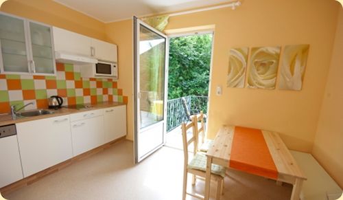 Svetlá kuchyňa s jedálenským kútom, farebným obkladom a otvorenými balkónovými dverami.