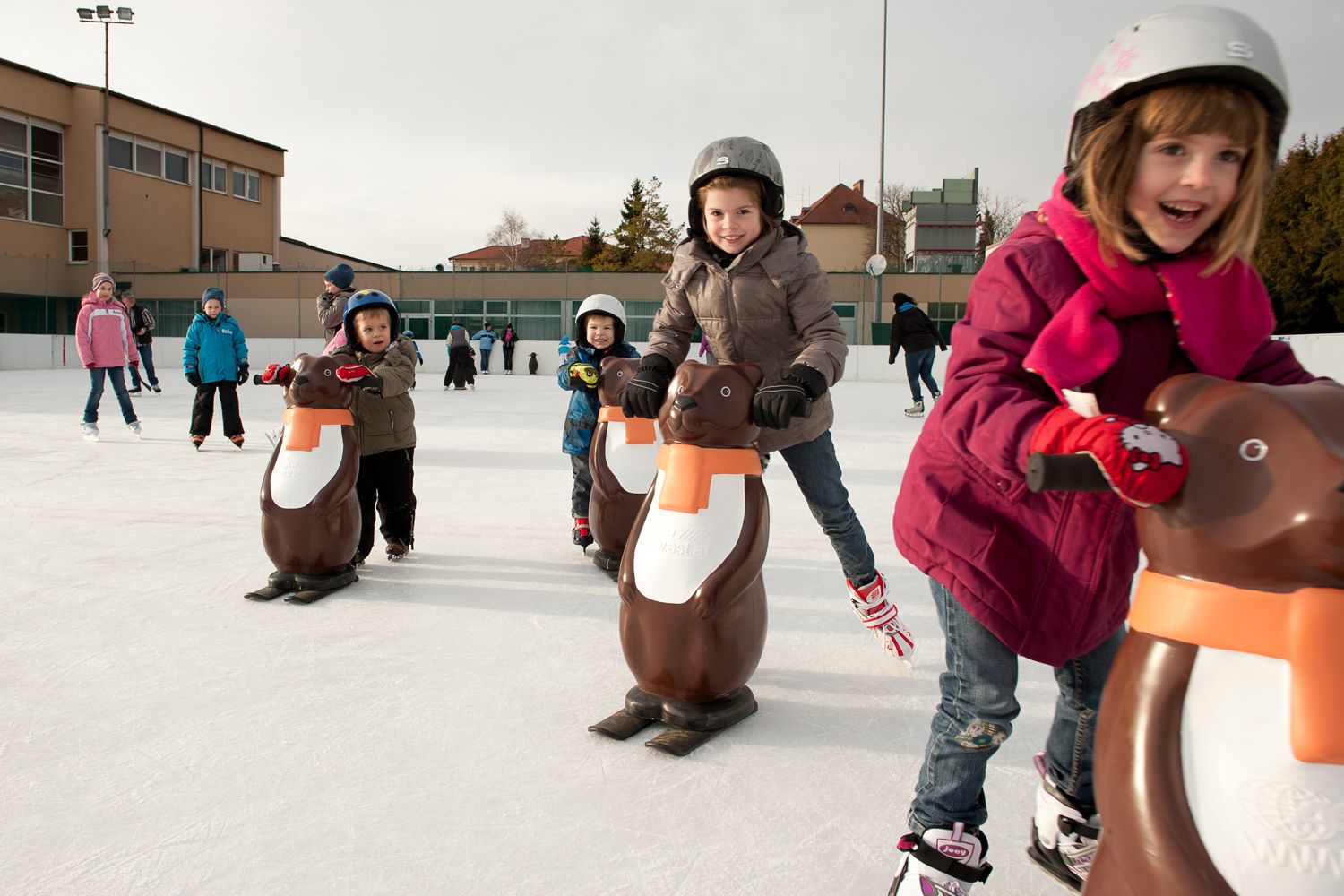 Deti korčuľujúce s pomôckami tučniakov na klzisku.