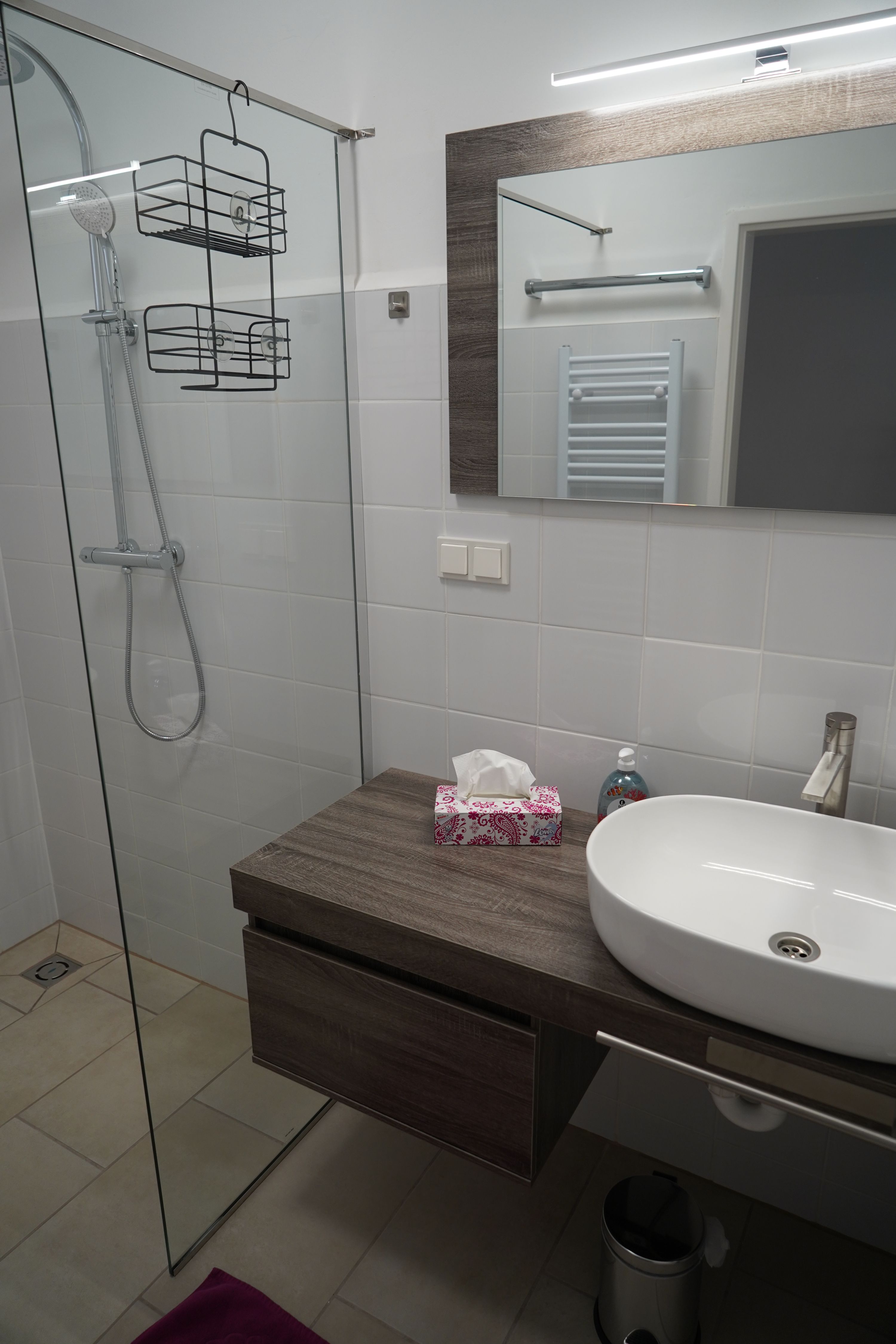 Moderná kúpeľňa so skleneným sprchovacím kútom, umývadlom a zrkadlom.