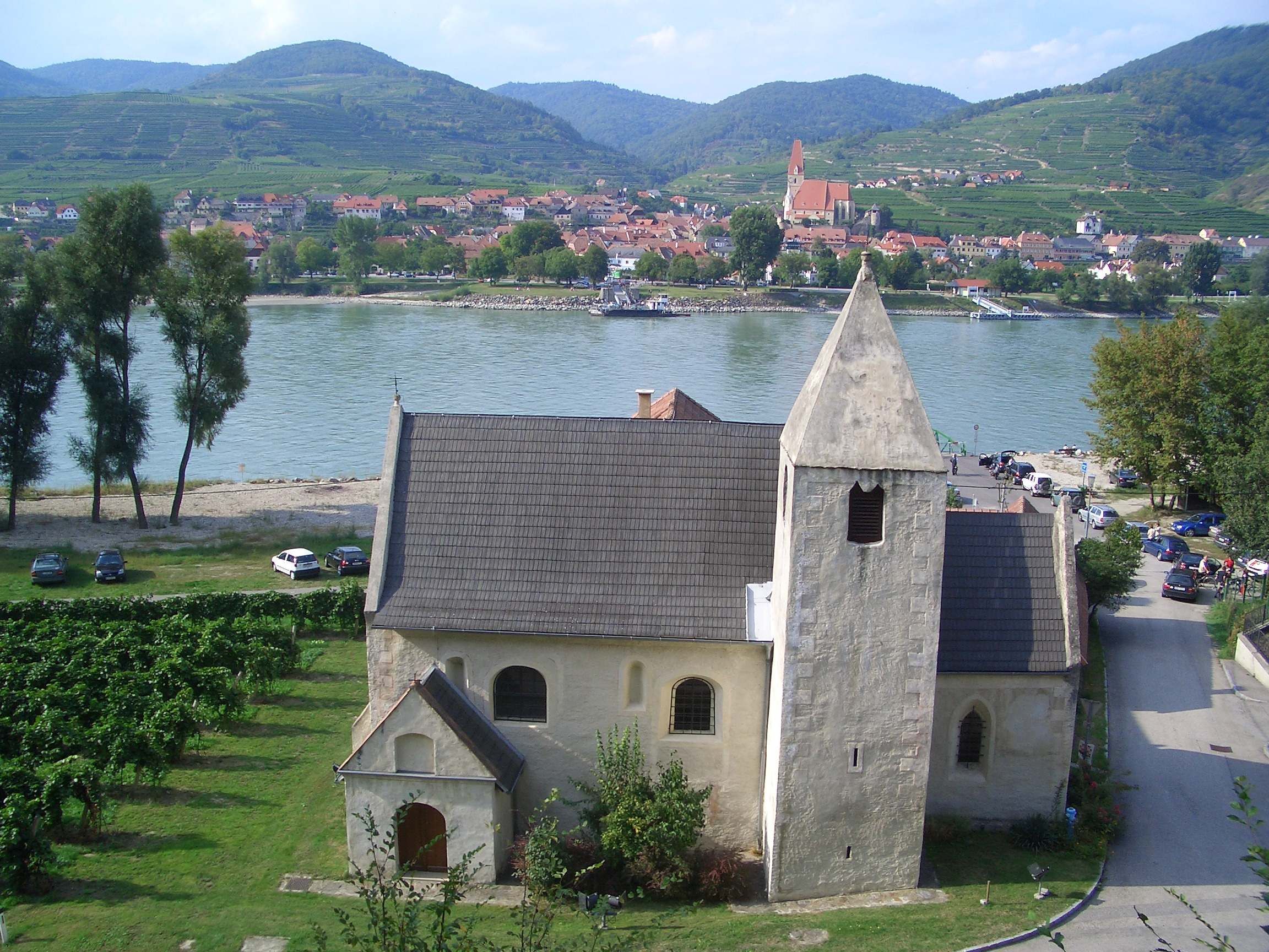 Kostol svätého Lorenza s riekou a dedinou v pozadí.