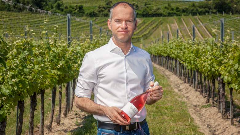 Muž vo vinici s fľašou ružového vína.