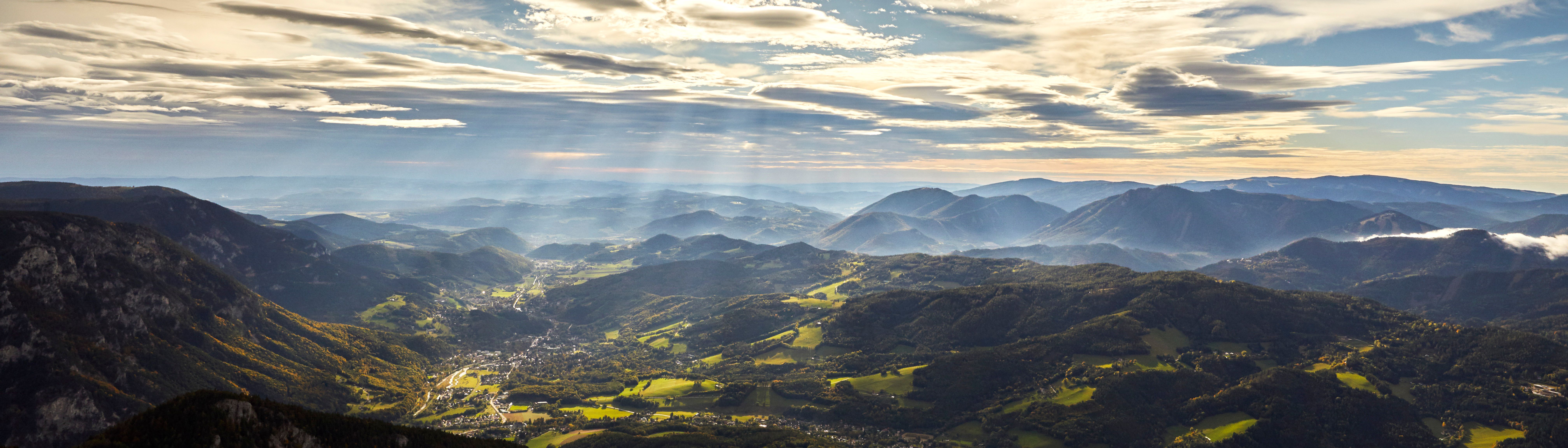 Panoramatický pohľad na Raxské Alpy so slnečnými lúčmi a mrakmi na oblohe.