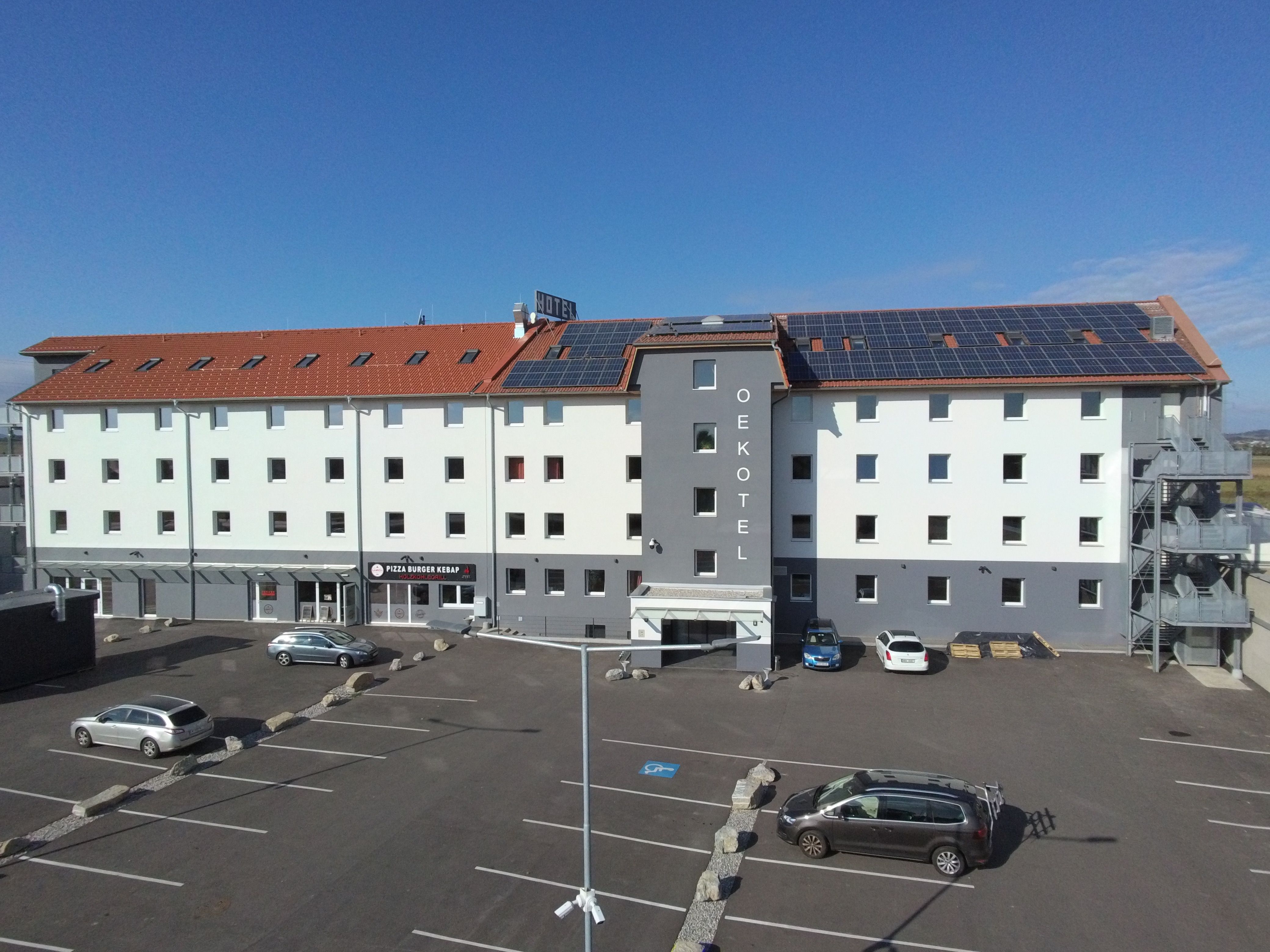 OEKOTEL Föhrenhain so solárnymi panelmi na streche a parkoviskom pred budovou.