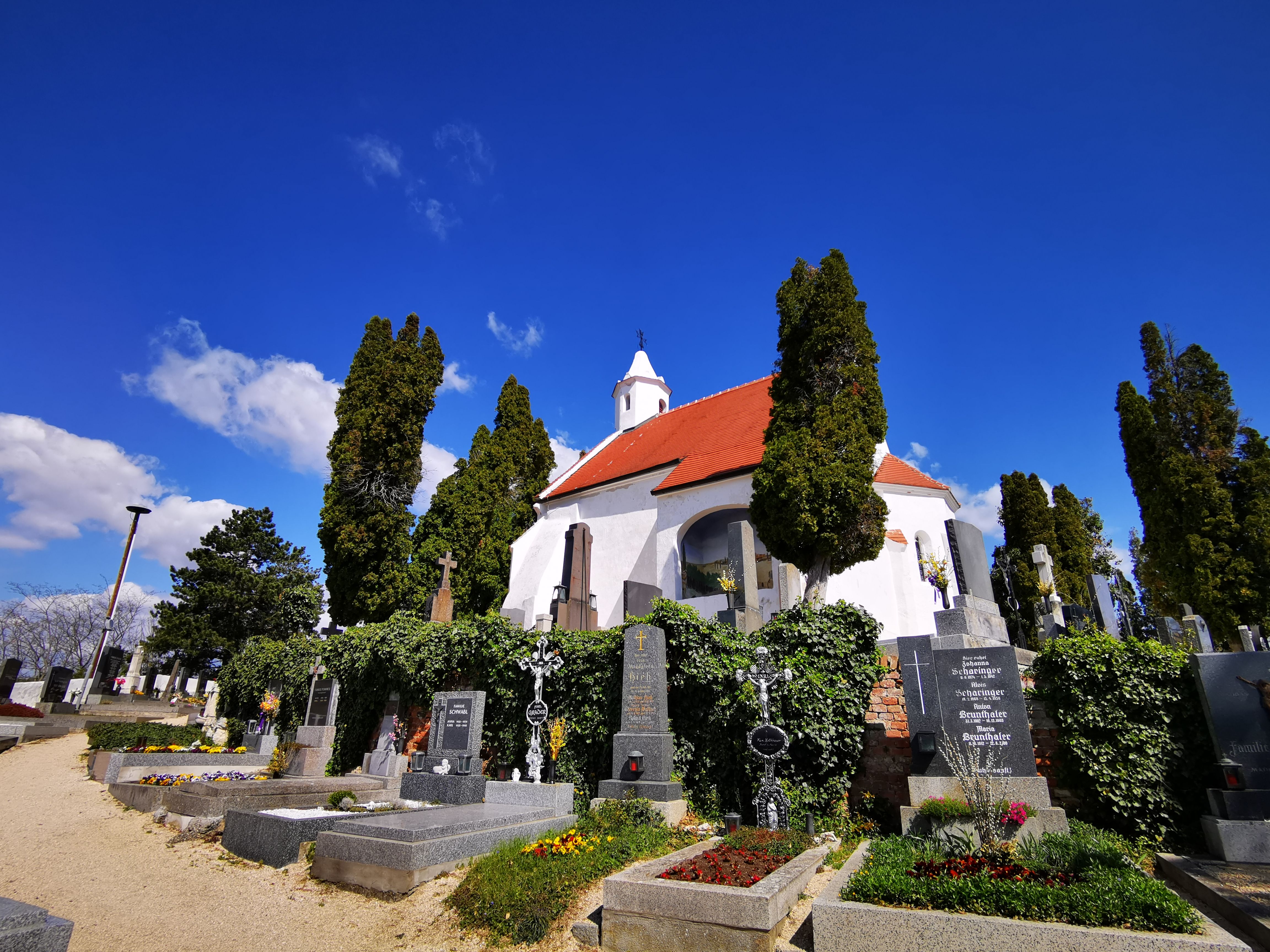 Kostol Kunigungenkirche v Mailbergu s cintorínom a kvitnúcimi hrobmi v popredí.