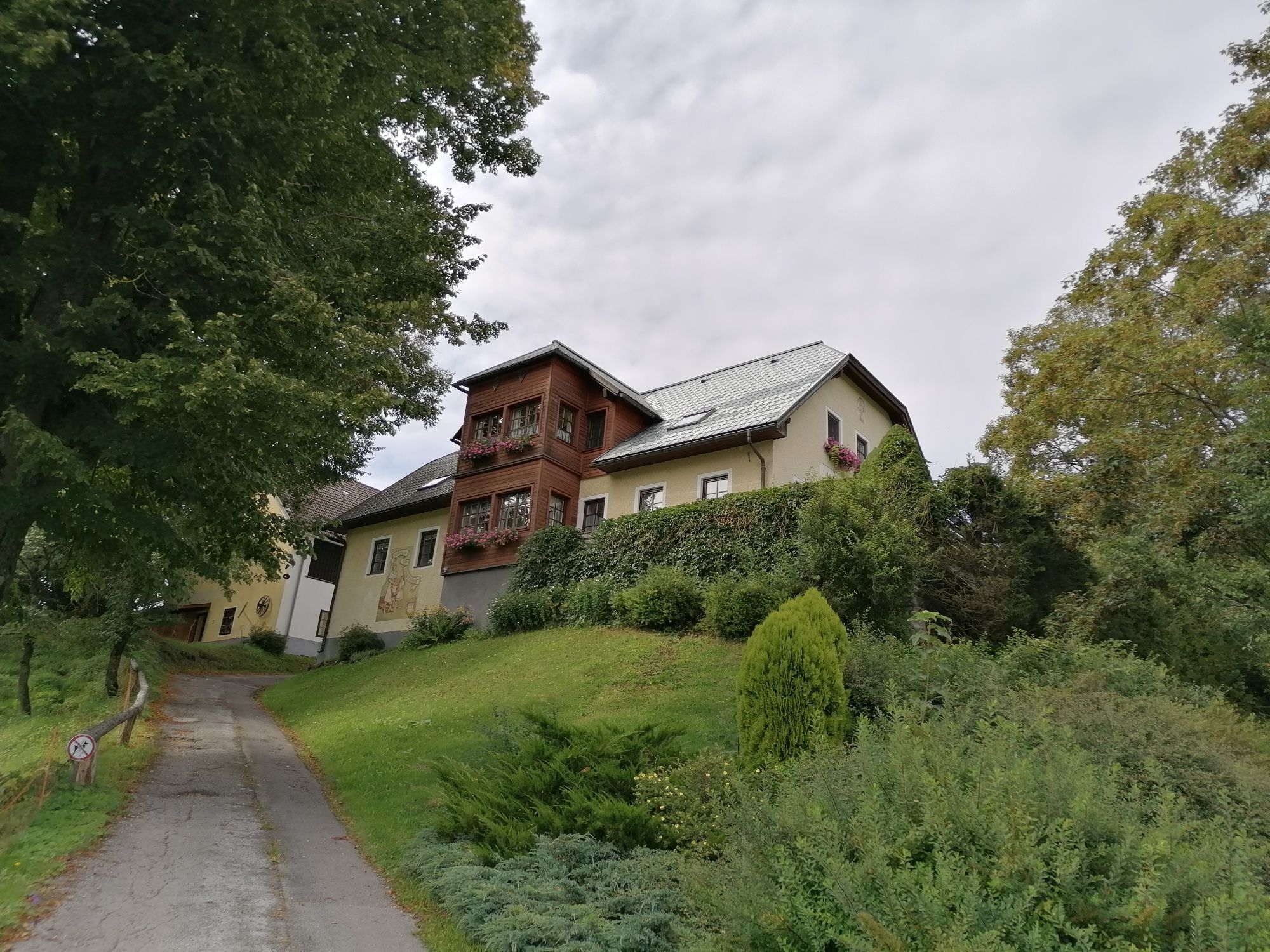 Veľký dom na kopci so stromami a cestou v popredí.