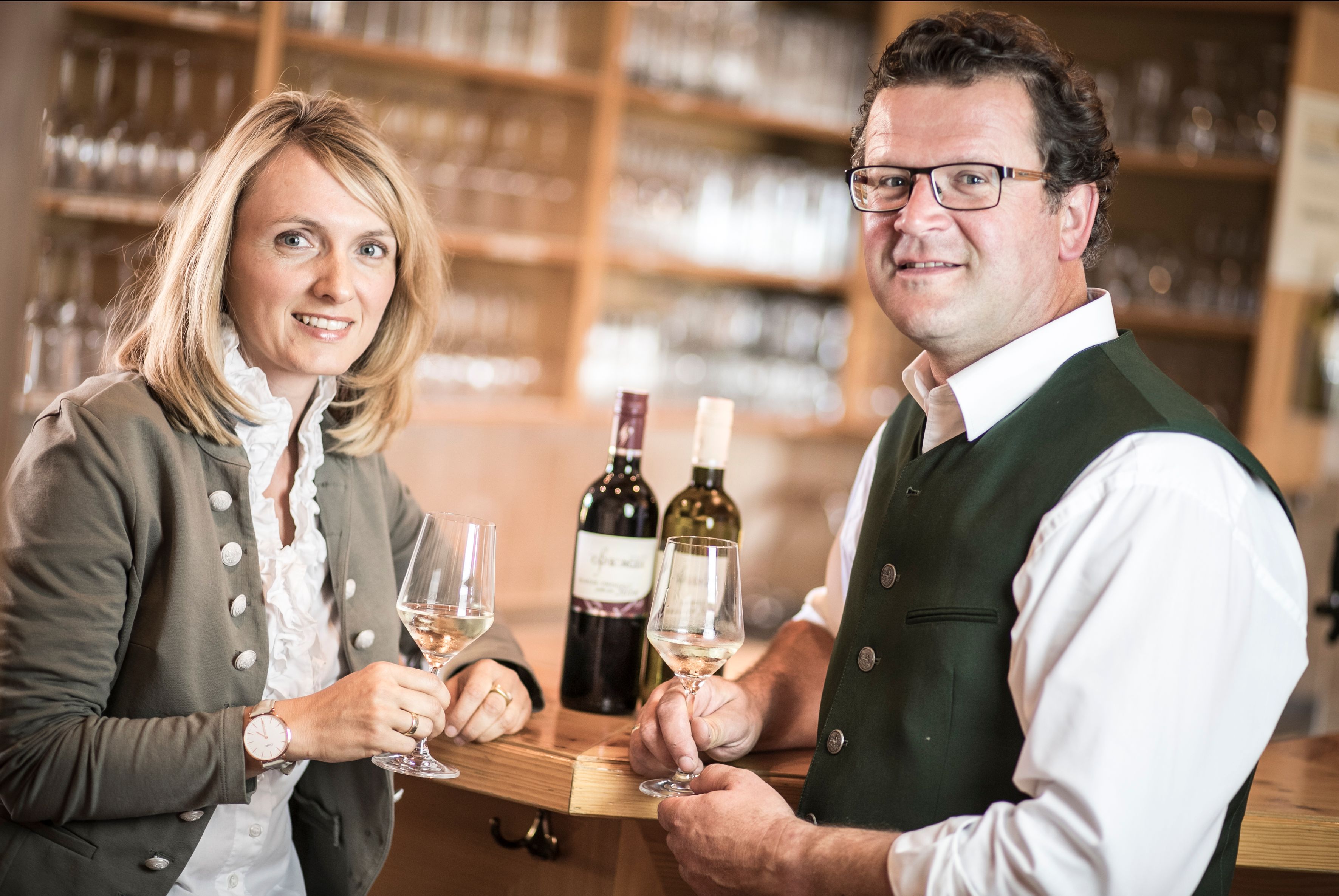 Dvaja ľudia v tradičnom odeve držia poháre na víno vo vinárni.