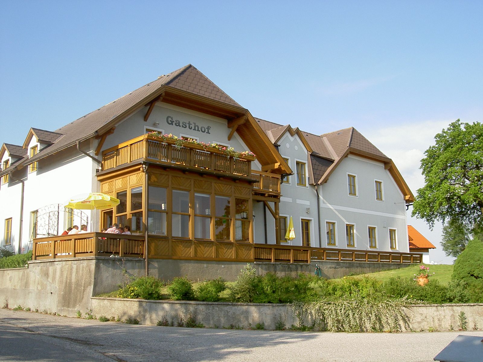 Tradičný hostinec s drevenou verandou a kvetmi na balkóne, obklopený zelenou krajinou.