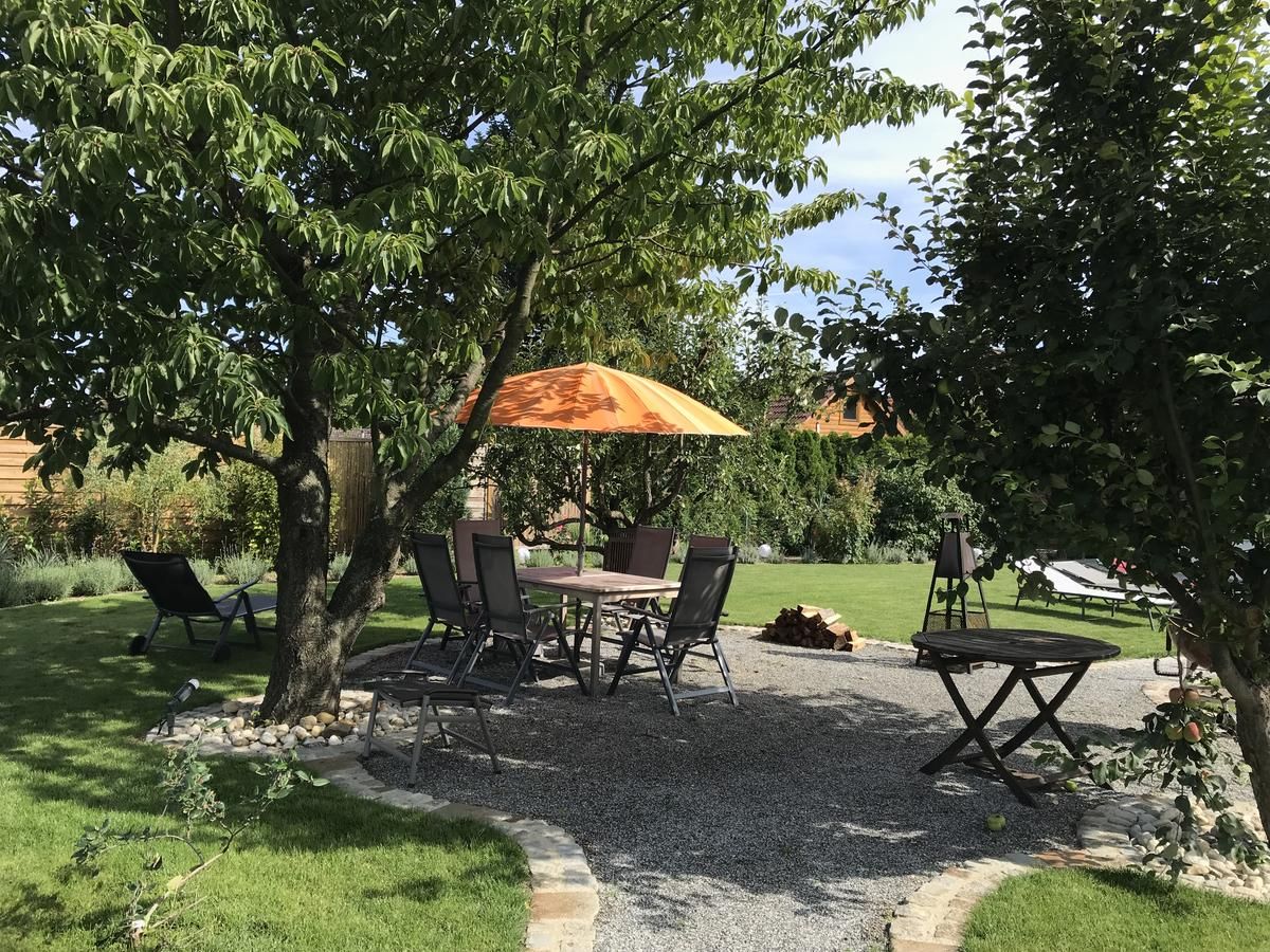 Záhrada s posedením pod stromami, stôl a stoličky, oranžový slnečník.