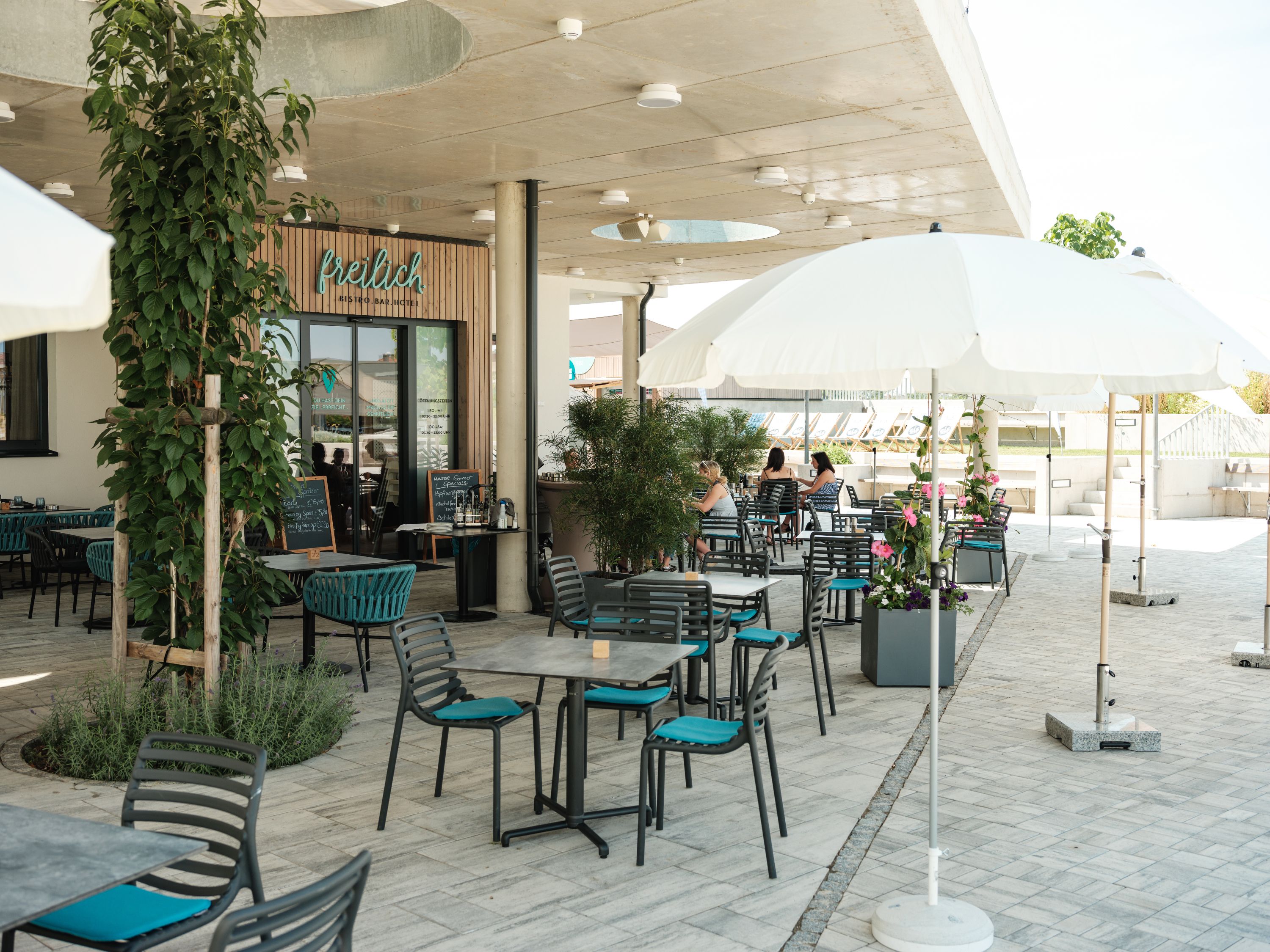 Vonkajší priestor kaviarne so stolmi, stoličkami a slnečníkmi.