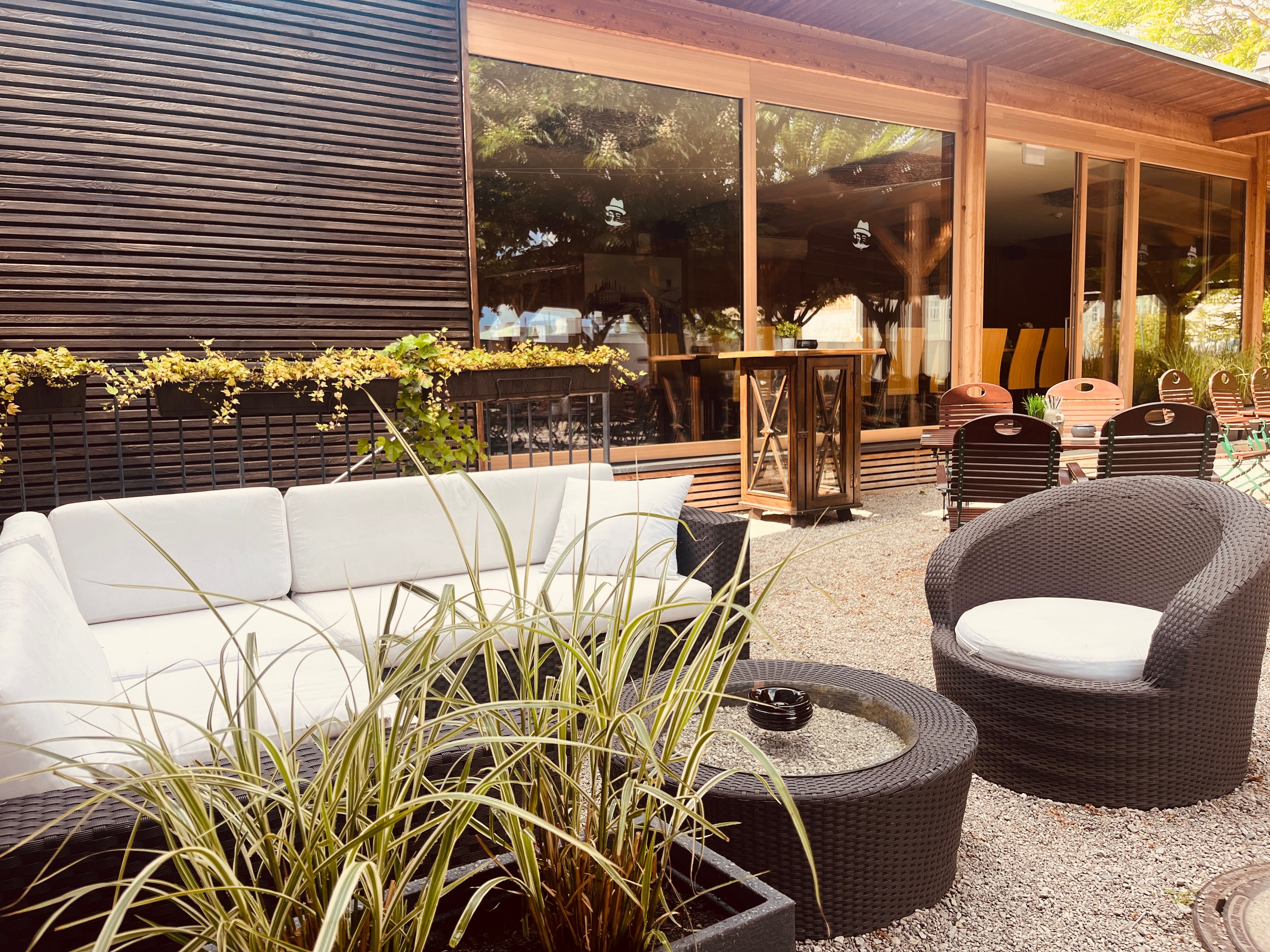 Útulný vonkajší salónik s bielymi pohovkami, okrúhlymi stolmi a rastlinami.