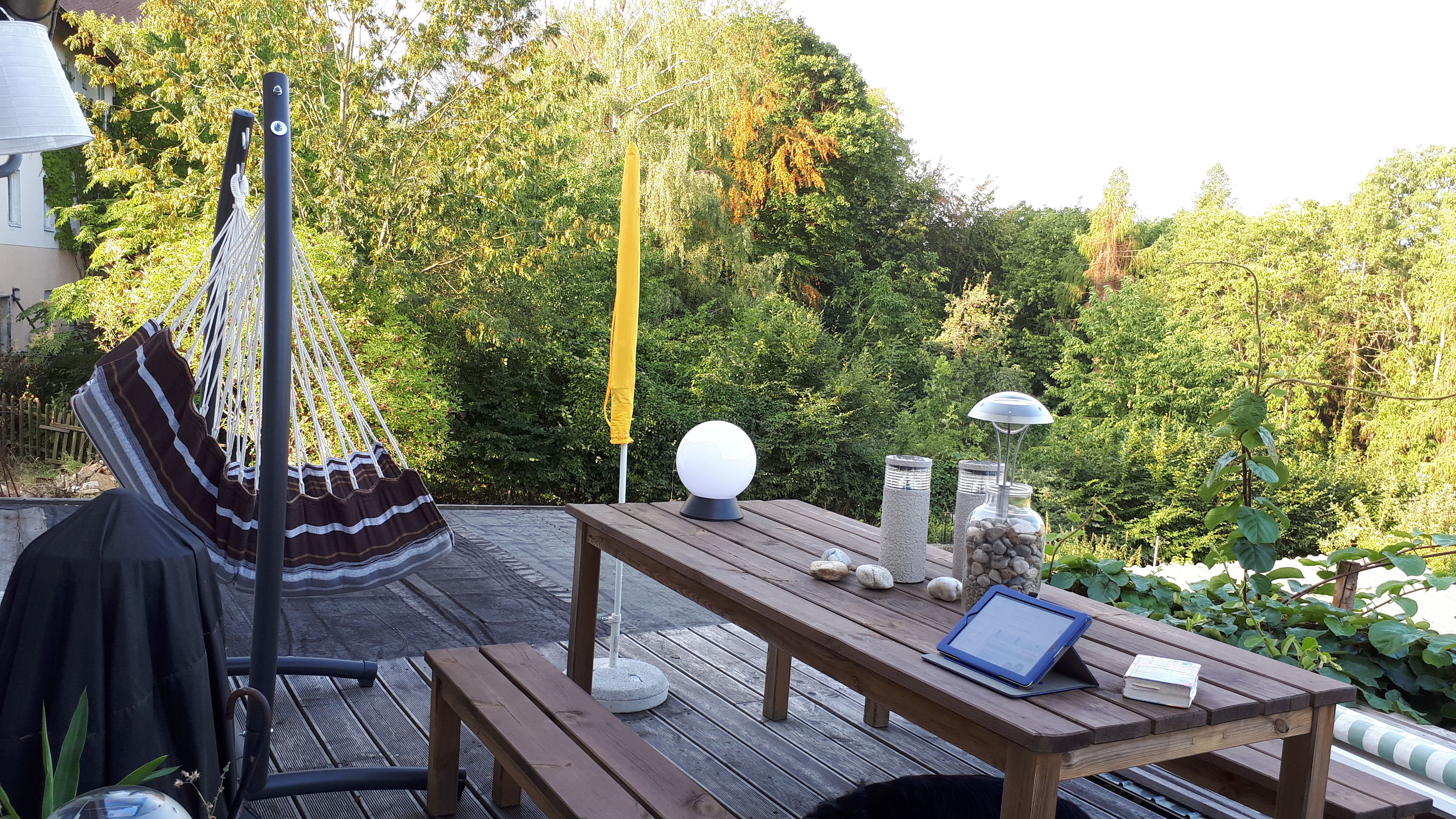 Terasa s hojdacou sieťou, dreveným stolom a výhľadom na zelené stromy.