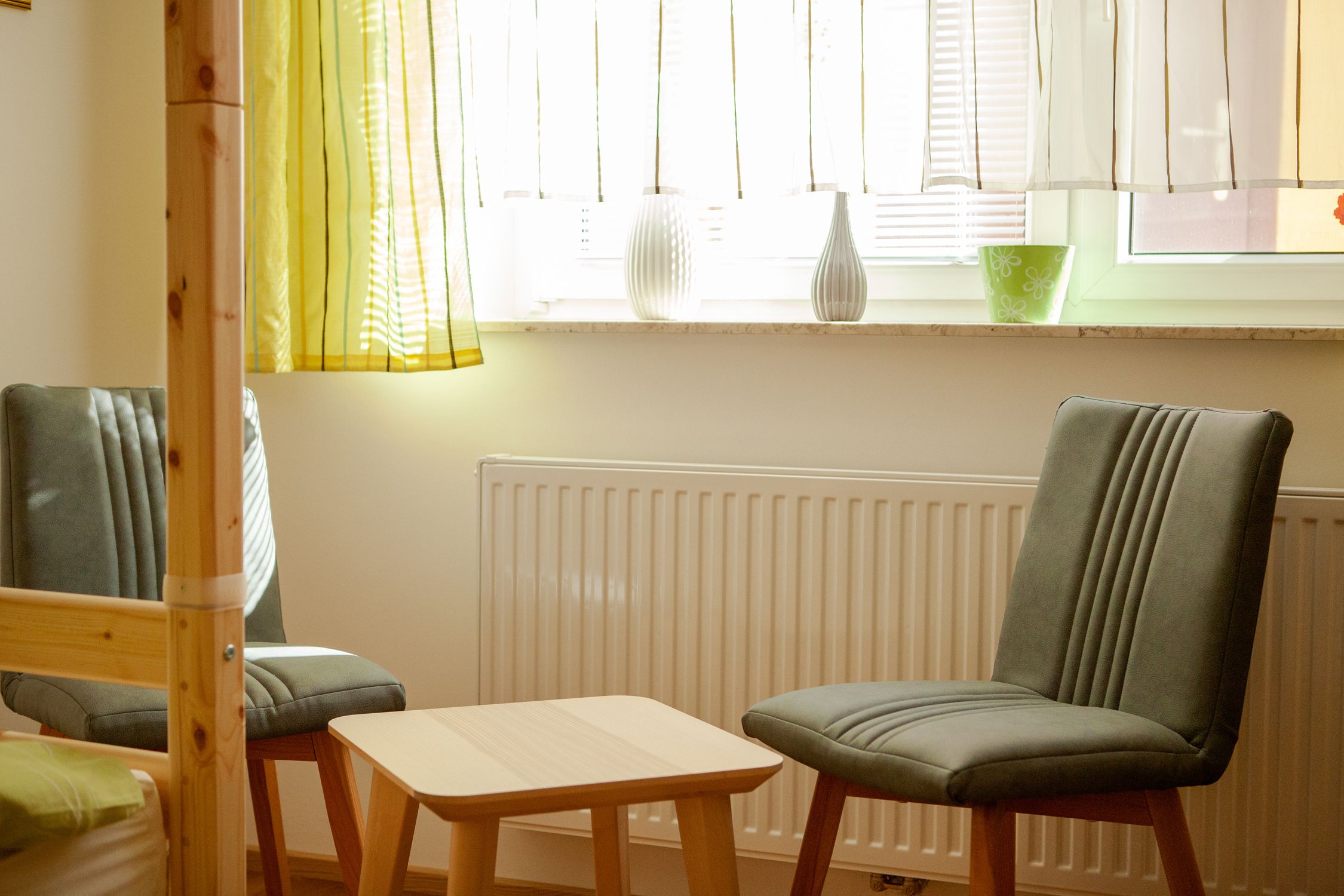 Dve sivé stoličky a malý drevený stolík pred oknom so závesmi v spálni.