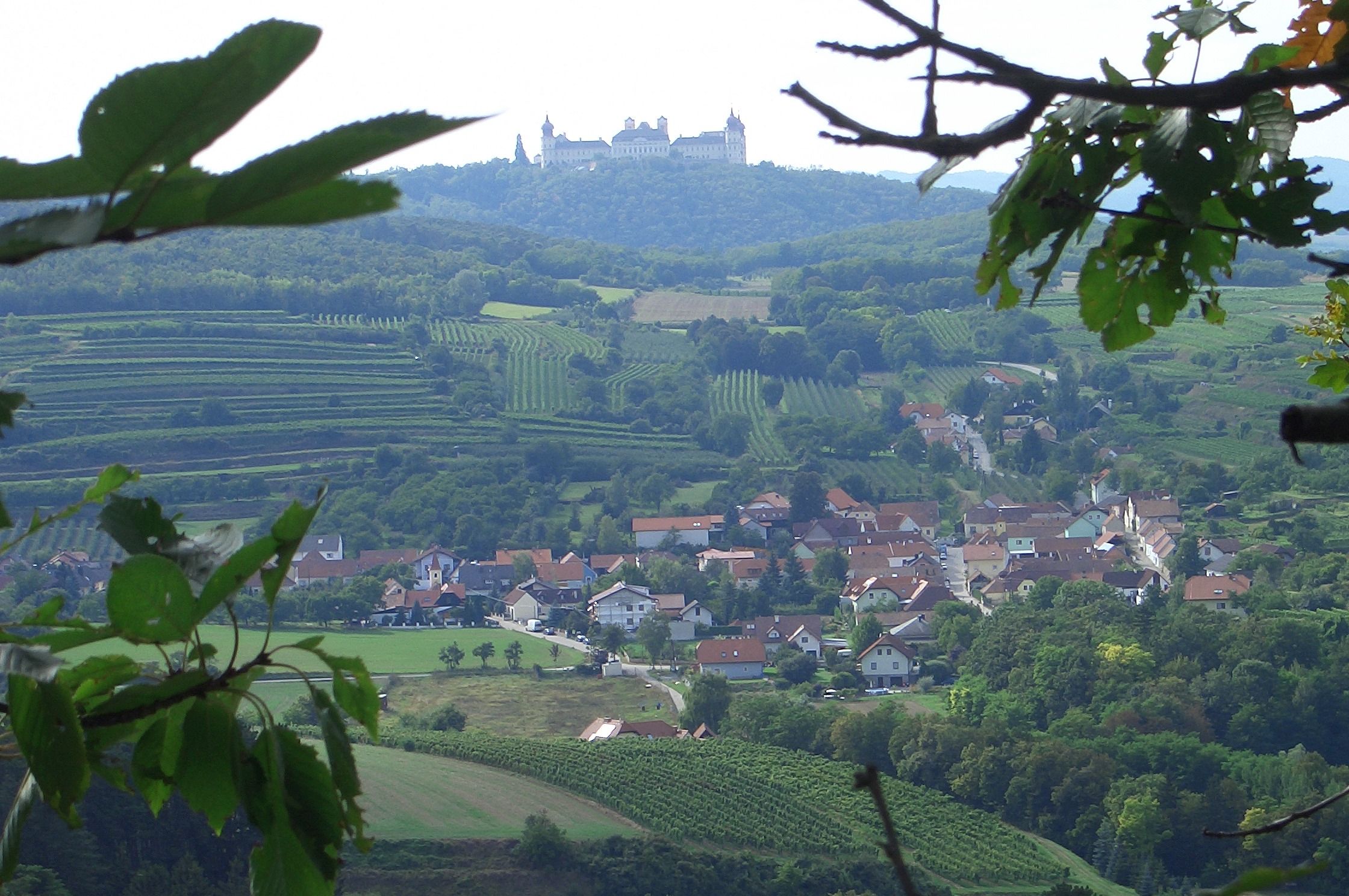 Pohľad na opátstvo Göttweig na kopci, obklopené vinicami a dedinou v popredí.