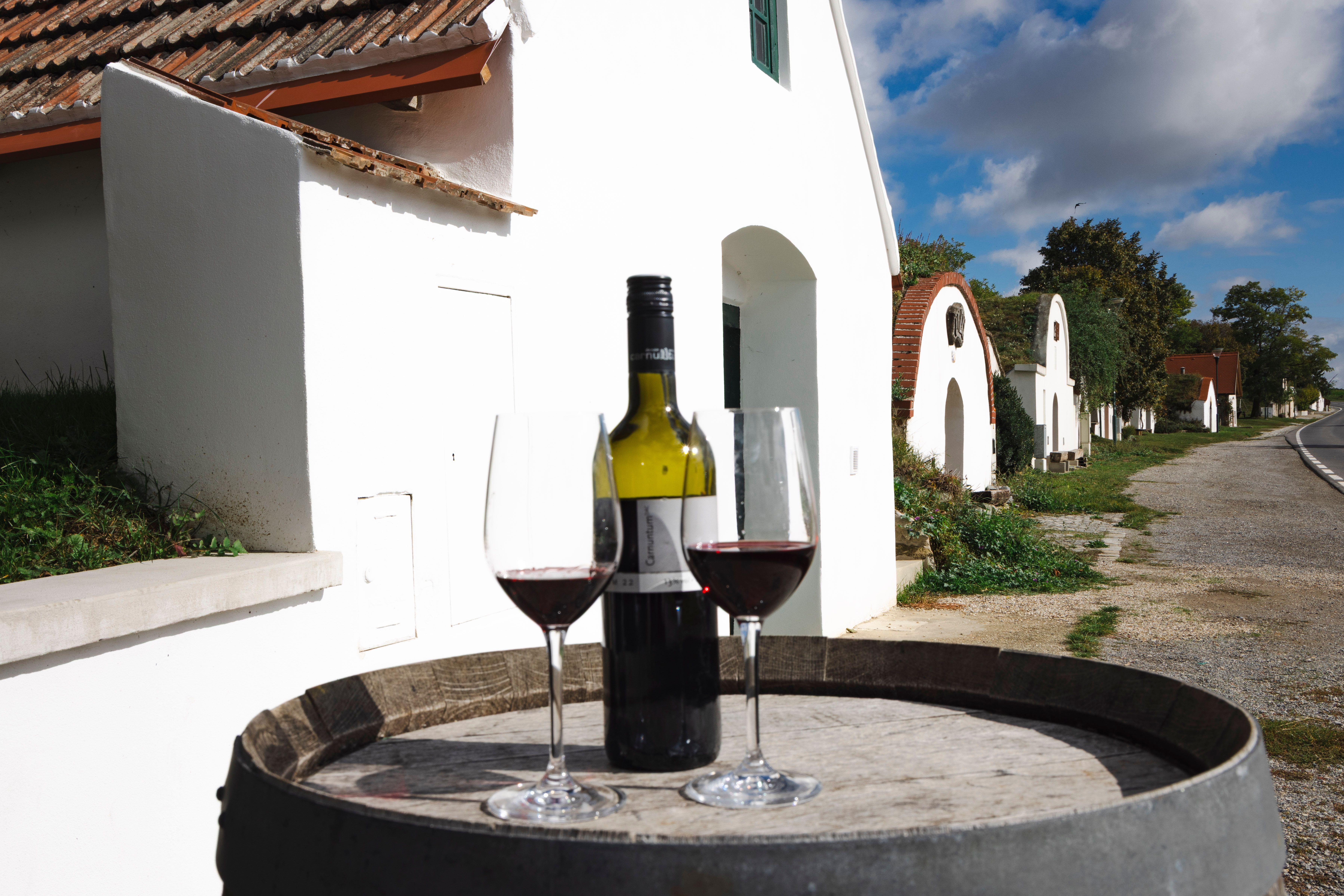 Dva poháre na víno a fľaša červeného vína na sude s vínom, v pozadí Vínne uličky