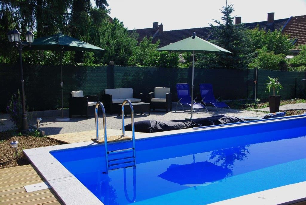Vonkajší priestor s modrým bazénom obklopený ležadlami, slnečníkmi a záhradným nábytkom.