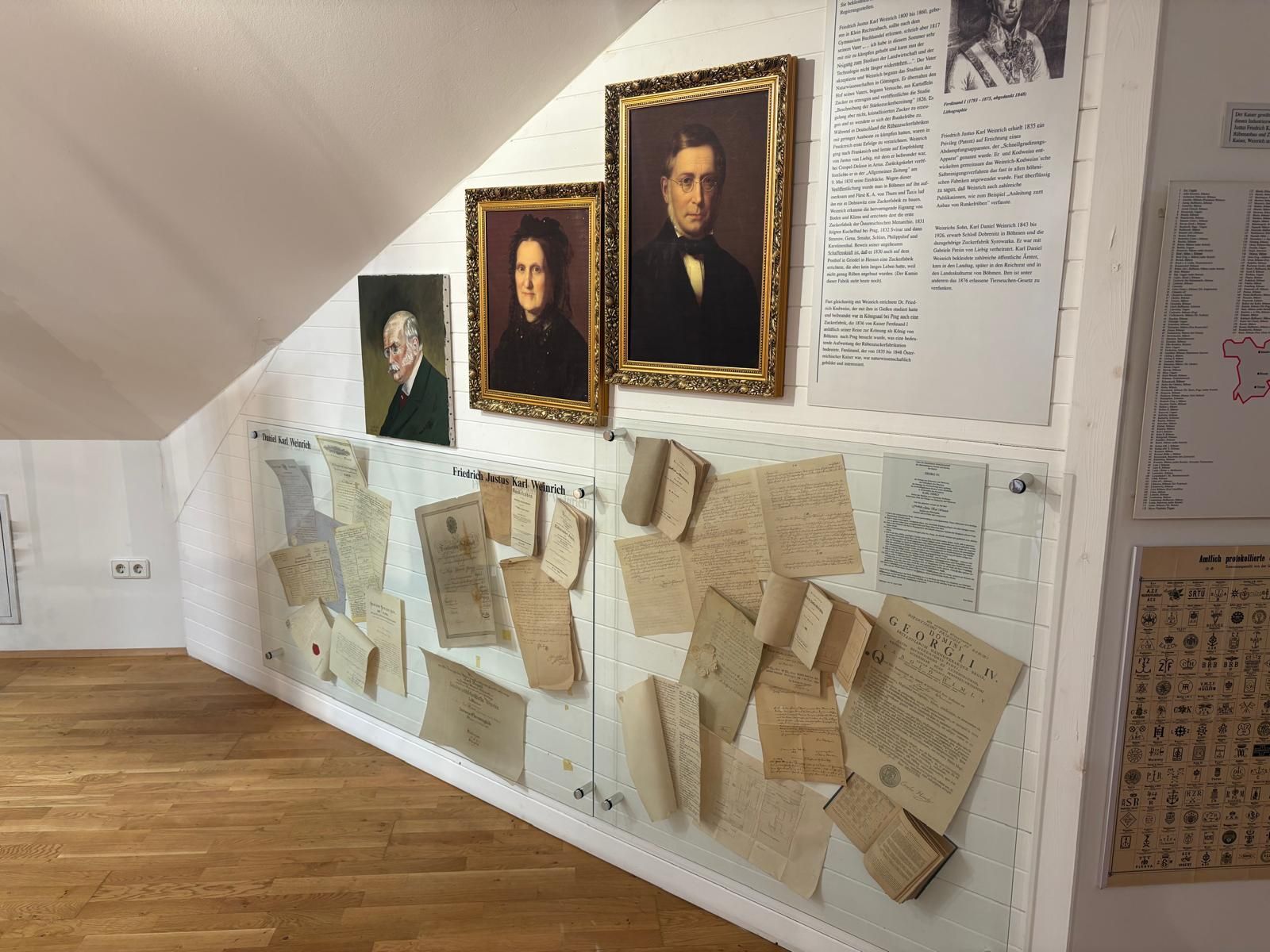 Výstava v Múzeu cukru s portrétmi a historickými dokumentmi na stene.