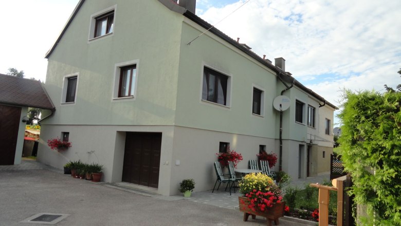 Exteri&eacute;rov&yacute; pohľad na dvojpodlažn&yacute; dom so zelenou farbou, kvetmi a z&aacute;hradn&yacute;m n&aacute;bytkom v popred&iacute;.