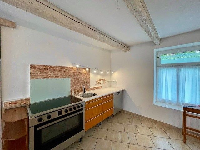 Moderná kuchyňa so sporákom, drevenými skrinkami a dláždenou podlahou.