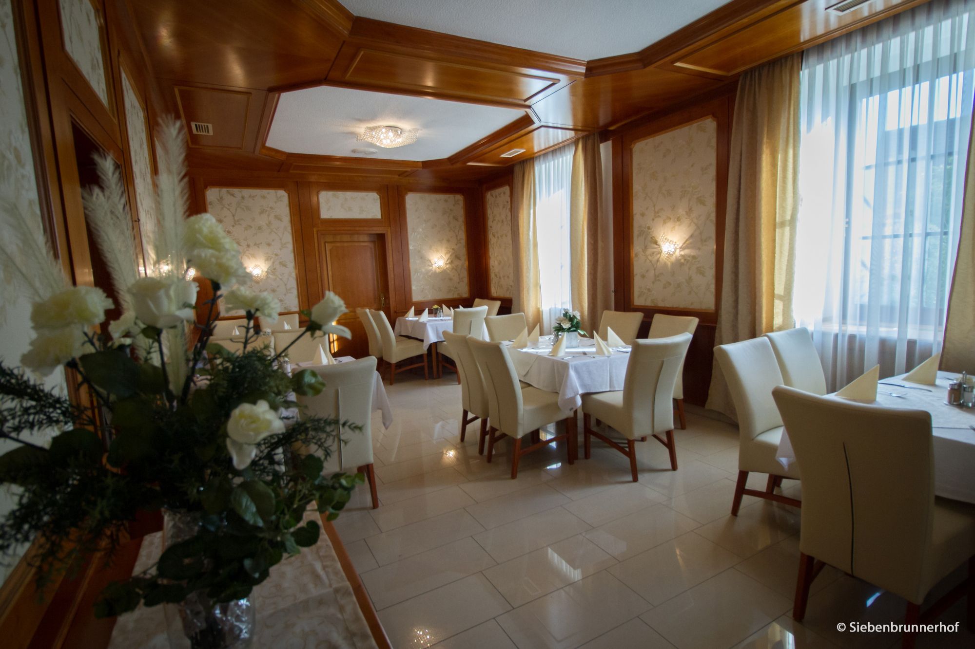 Elegantná jedáleň s prestretými stolmi, bielymi stoličkami a kvetinovou výzdobou.