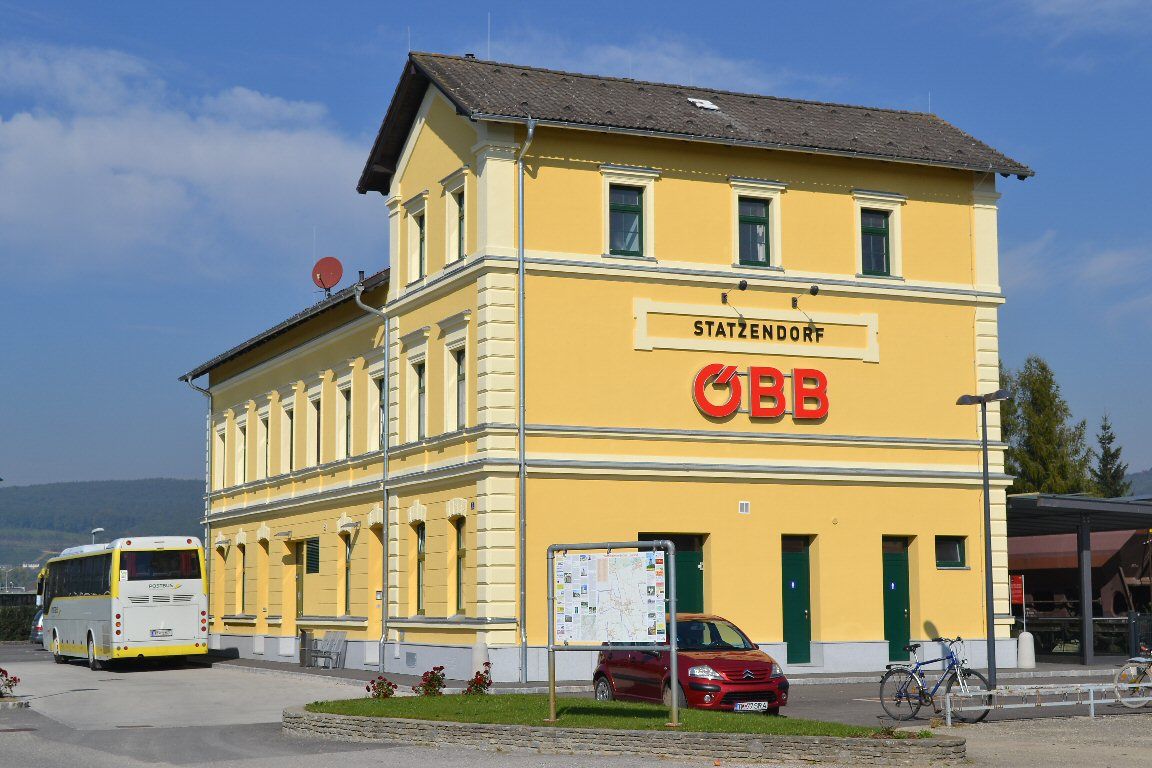 Žltá budova železničnej stanice s logom ÖBB a autobusom v popredí.