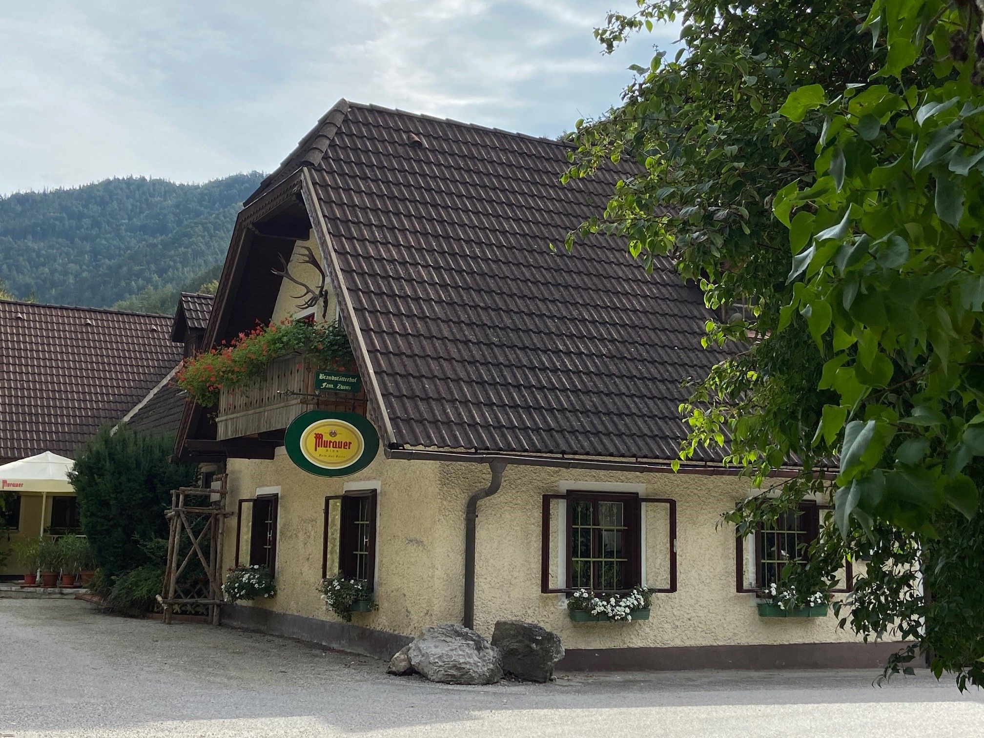 Tradičný hostinec s kvetmi a nápisom Murauer, obklopený stromami.