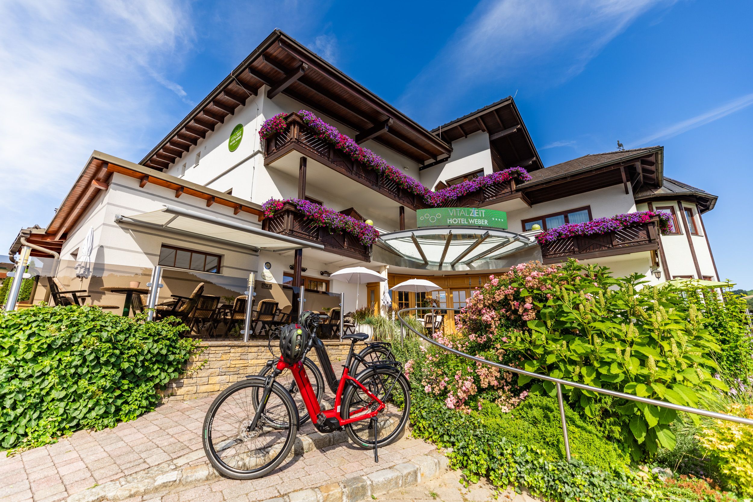 Exteriérový pohľad na hotel Vitalzeit Weber s kvetmi a bicyklom.