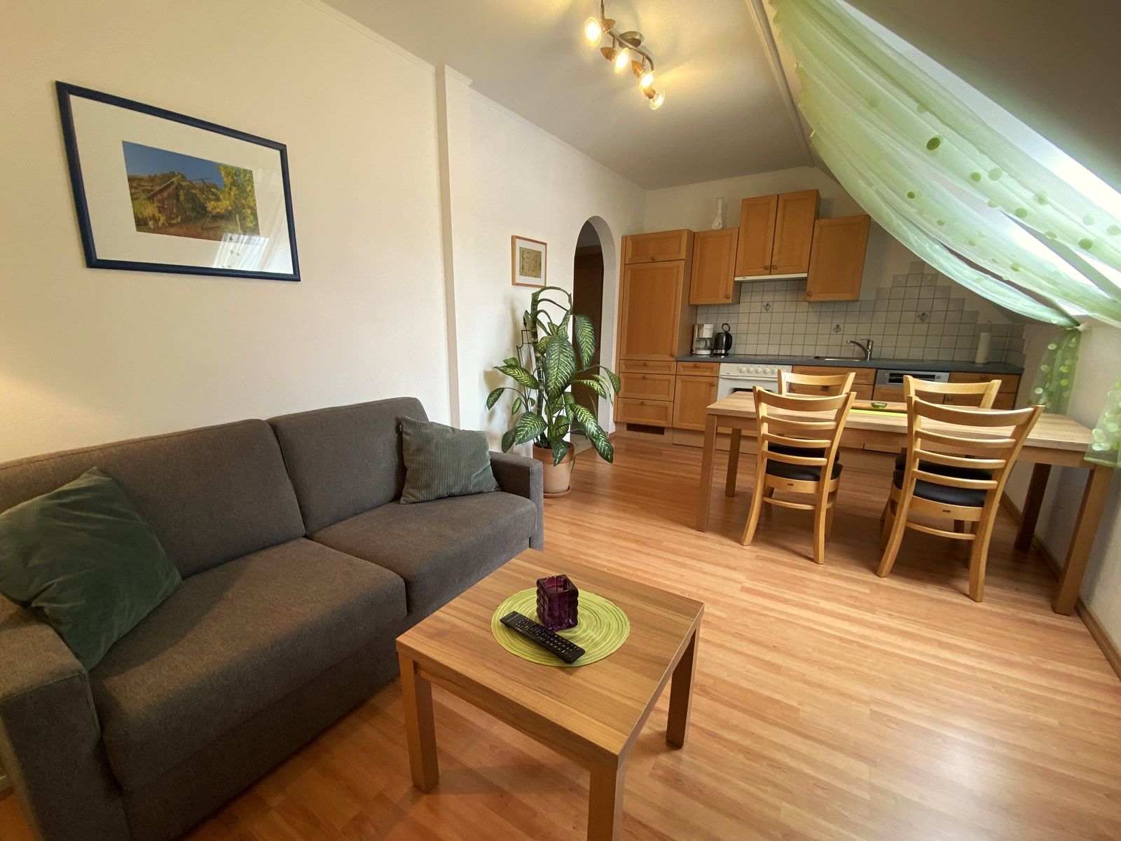 Obývacia izba so sivou pohovkou, dreveným stolom, jedálenským stolom a kuchyňou v pozadí.