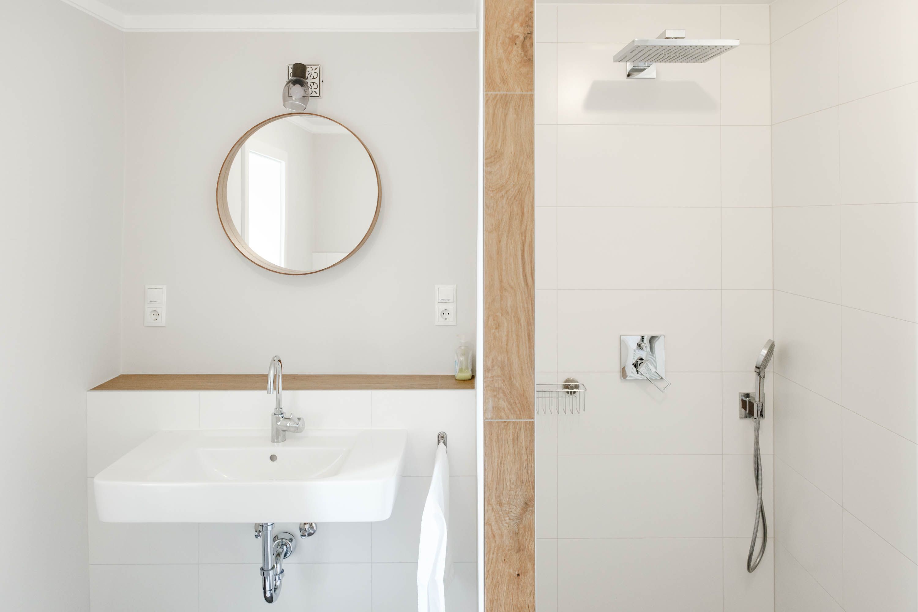 Moderná kúpeľňa s okrúhlym zrkadlom, umývadlom a sprchovacím kútom.