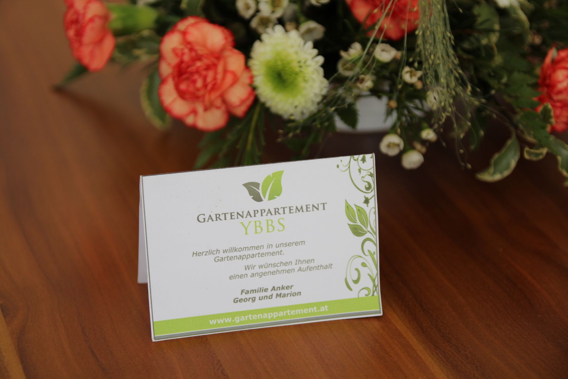 Uvítacia karta Gartenappartement Ybbs na stole s kvetmi.