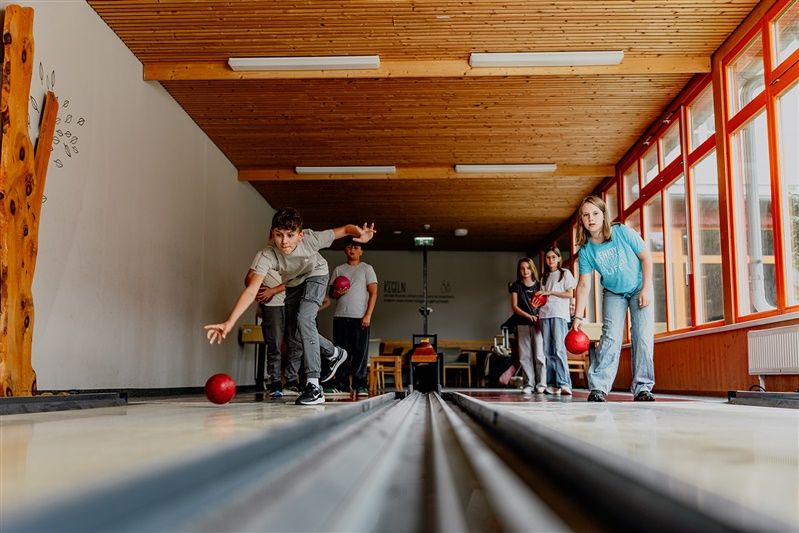 Deti hrajú kolky v miestnosti s drevenými stenami a veľkými oknami.