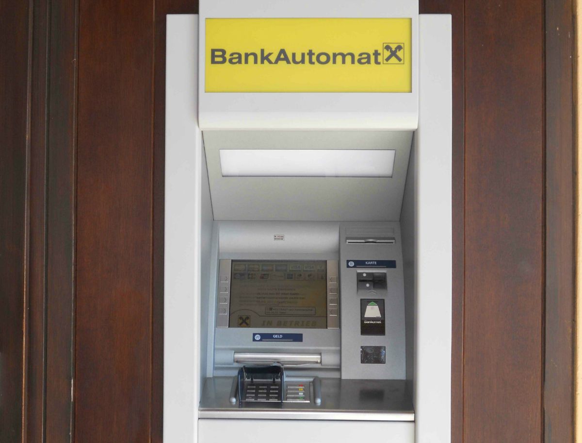 Bankomat so žltým nápisom a logom Raiffeisen.