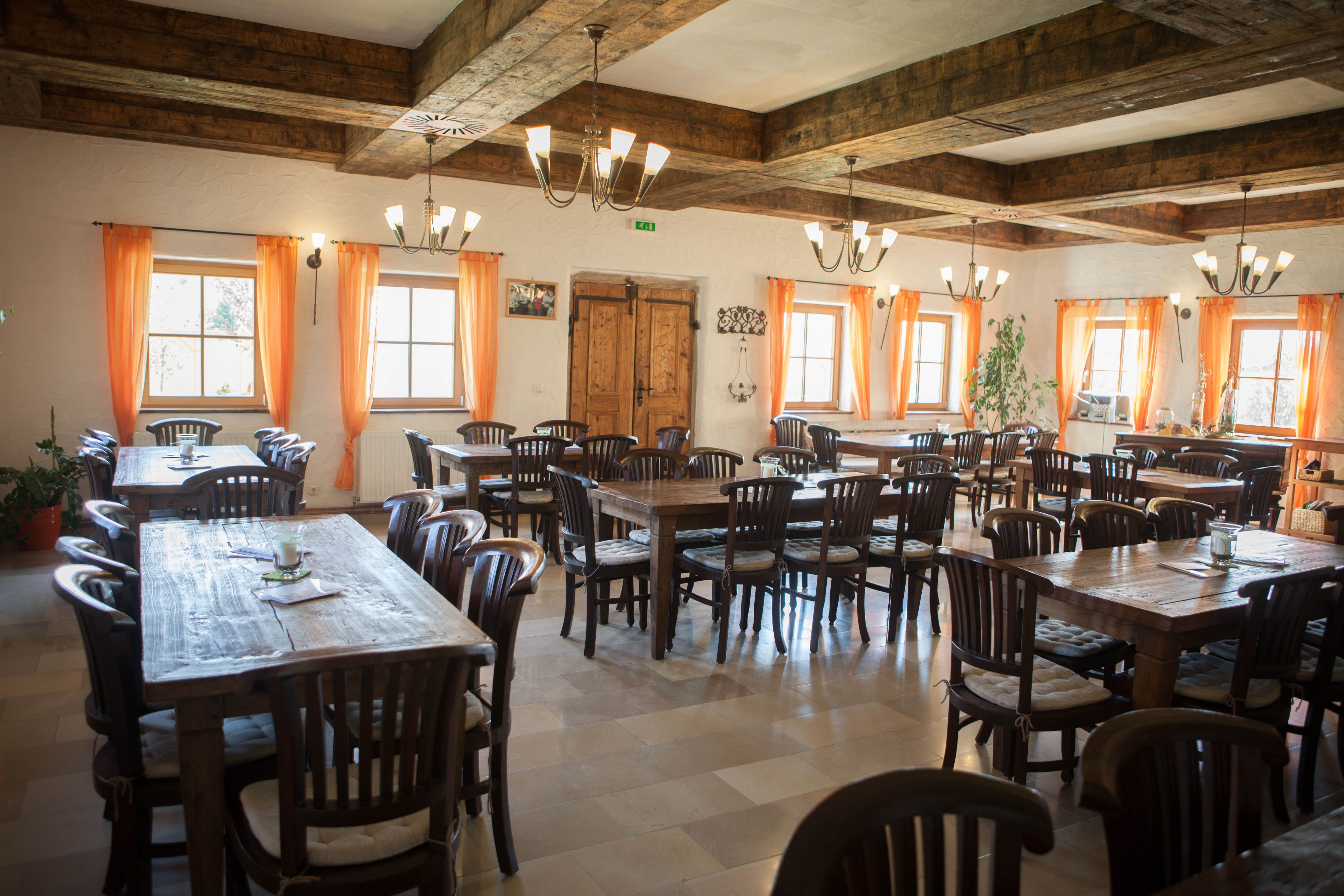 Rustikálna jedáleň s drevenými stolmi a stoličkami, oranžovými závesmi a dreveným trámovým stropom.