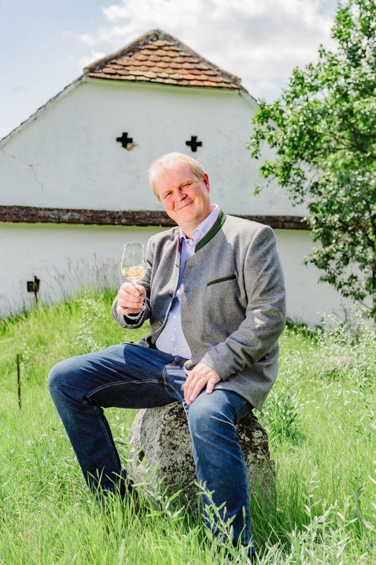 Muž sedí na kameni v prírode a v ruke drží pohár s vínom.