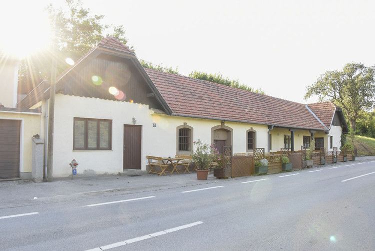 Tradičná budova s červenou škridlovou strechou a drevenými stolmi pred dverami, ktoré osvetľuje slnko.