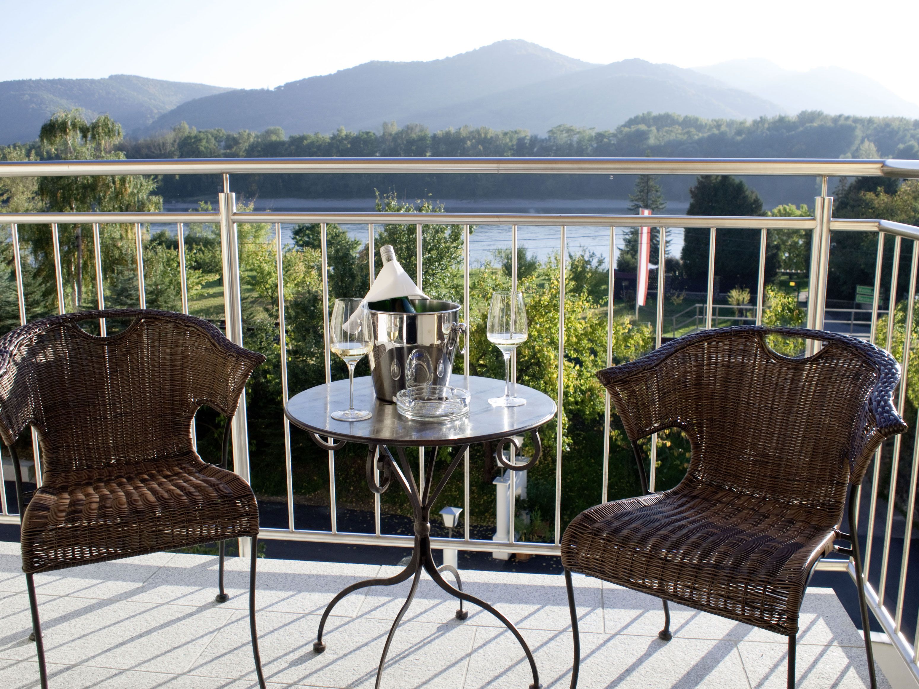 Dve ratanové kreslá a stôl s chladničkou na šampanské na terase s výhľadom na hory.